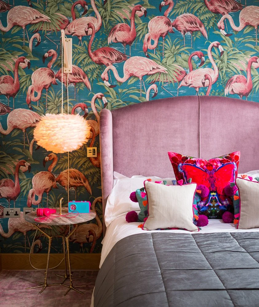 close up detail of pink headboard, flamingo wallpaper and lamp