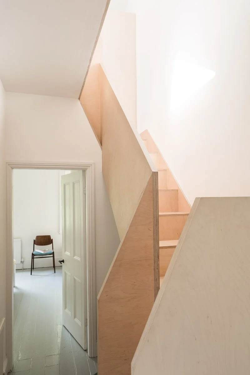 portrait photograph of birch ply staircase leading to a loft conversion, through a door a mid century wooden chair can be seen