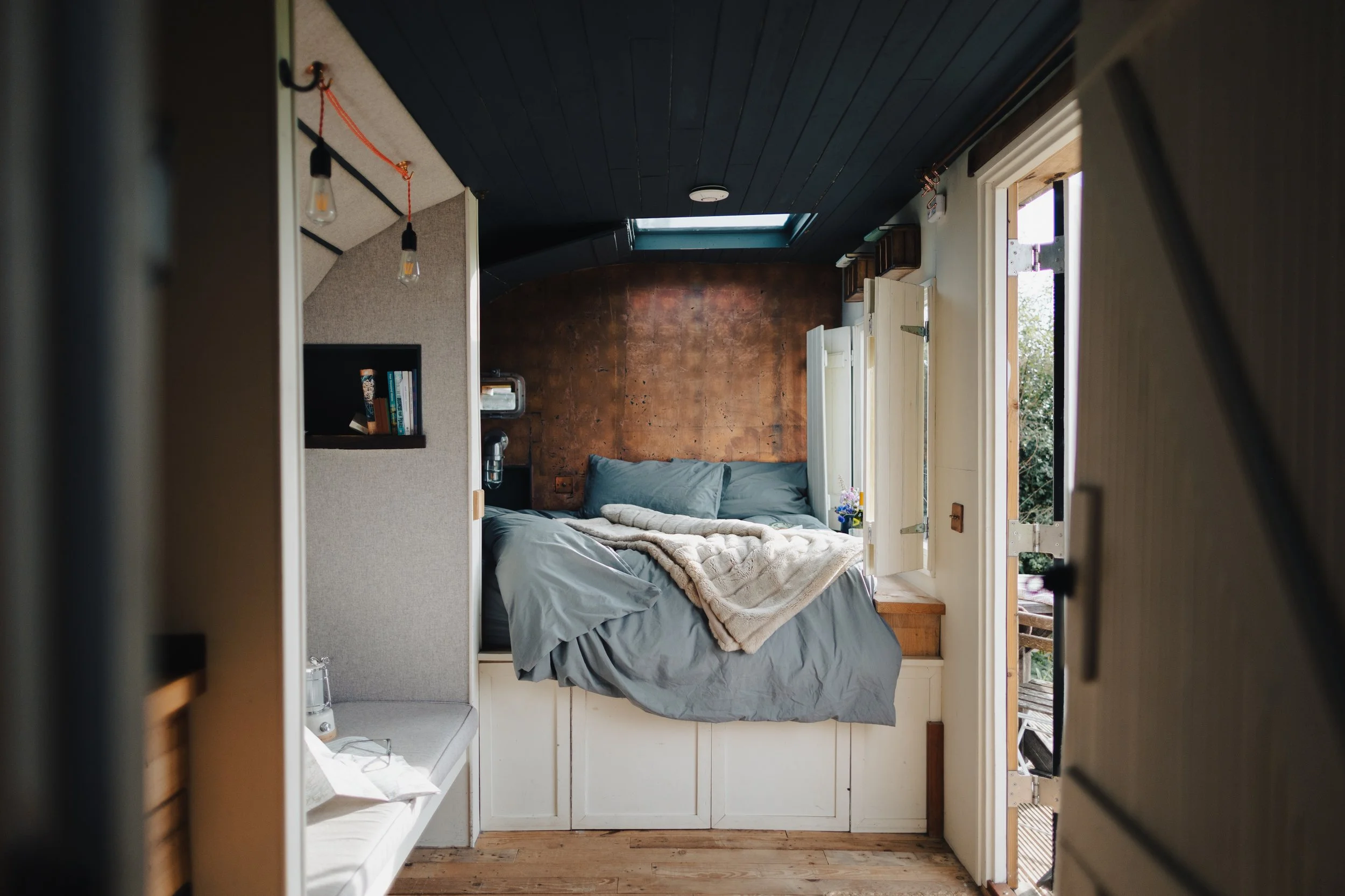 bedroom area to a shepherds hut with unmade bed, skylight in dark teal ceiling 