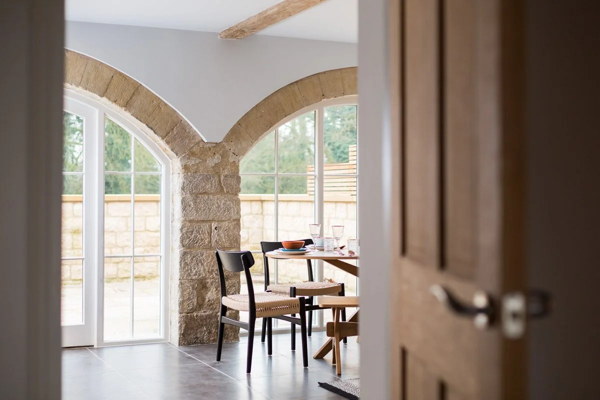 glimpse through doorway of dining table chairs and large arched windows, dark tile flooring 