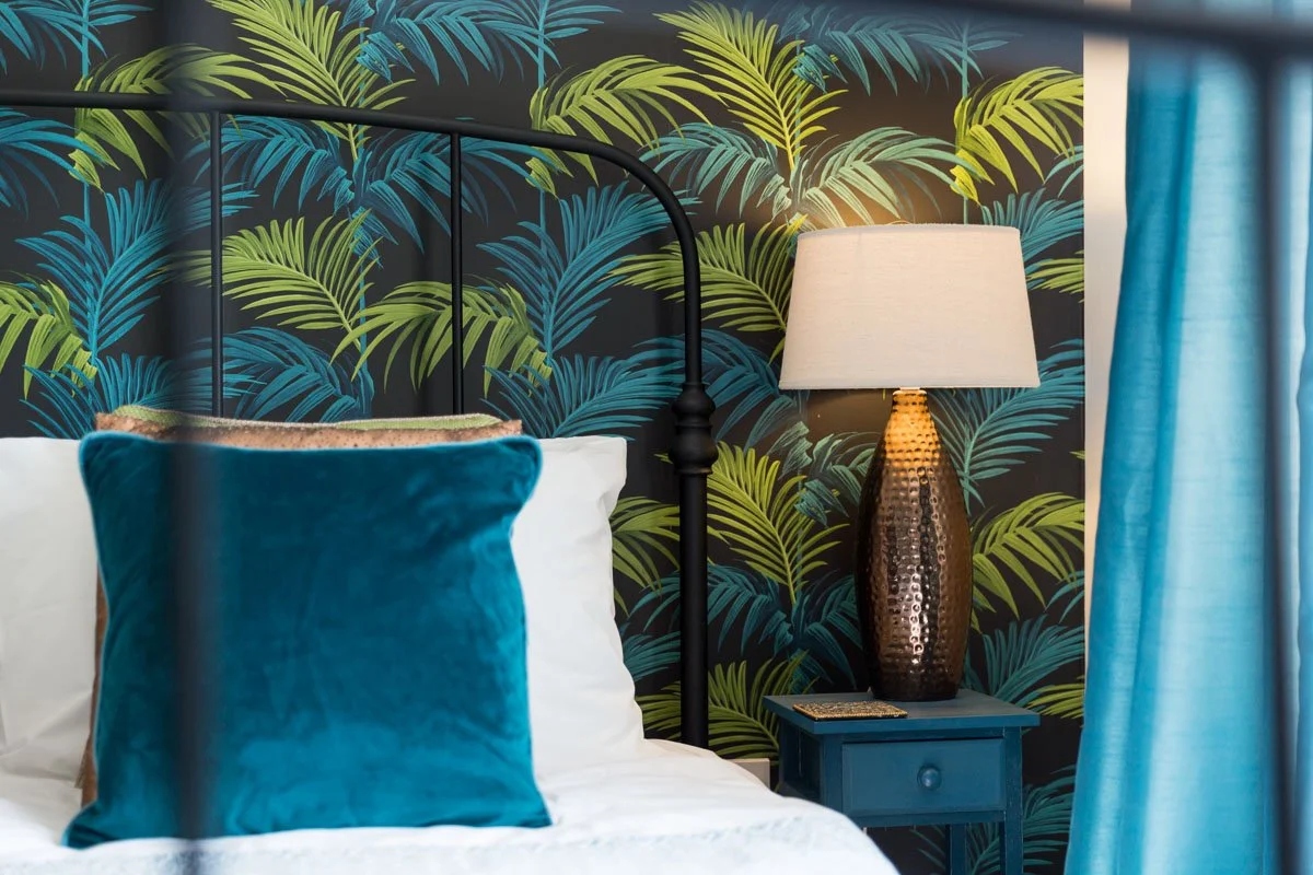 close up detail of black metal headboard with blue pillow, jungle wallpaper and lamp