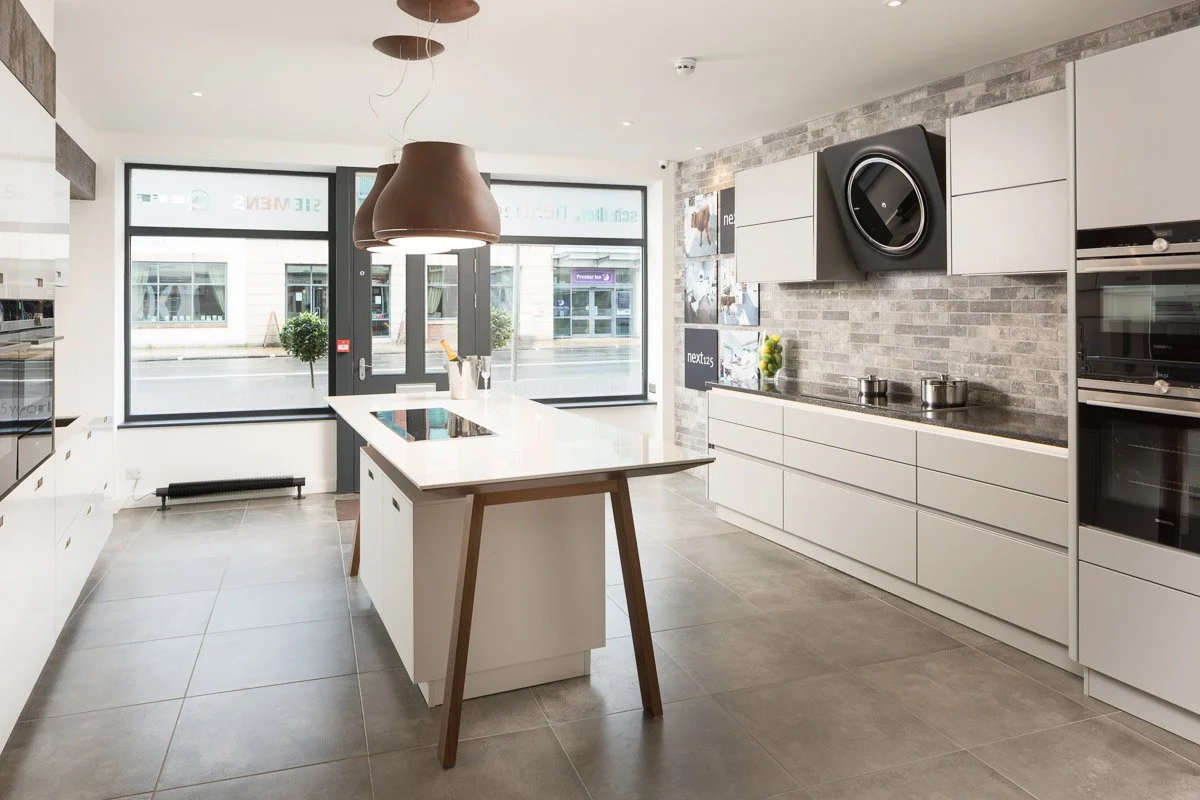 highly modern kitchen with white units and tops and dark tile flooring in studio 35 showroom
