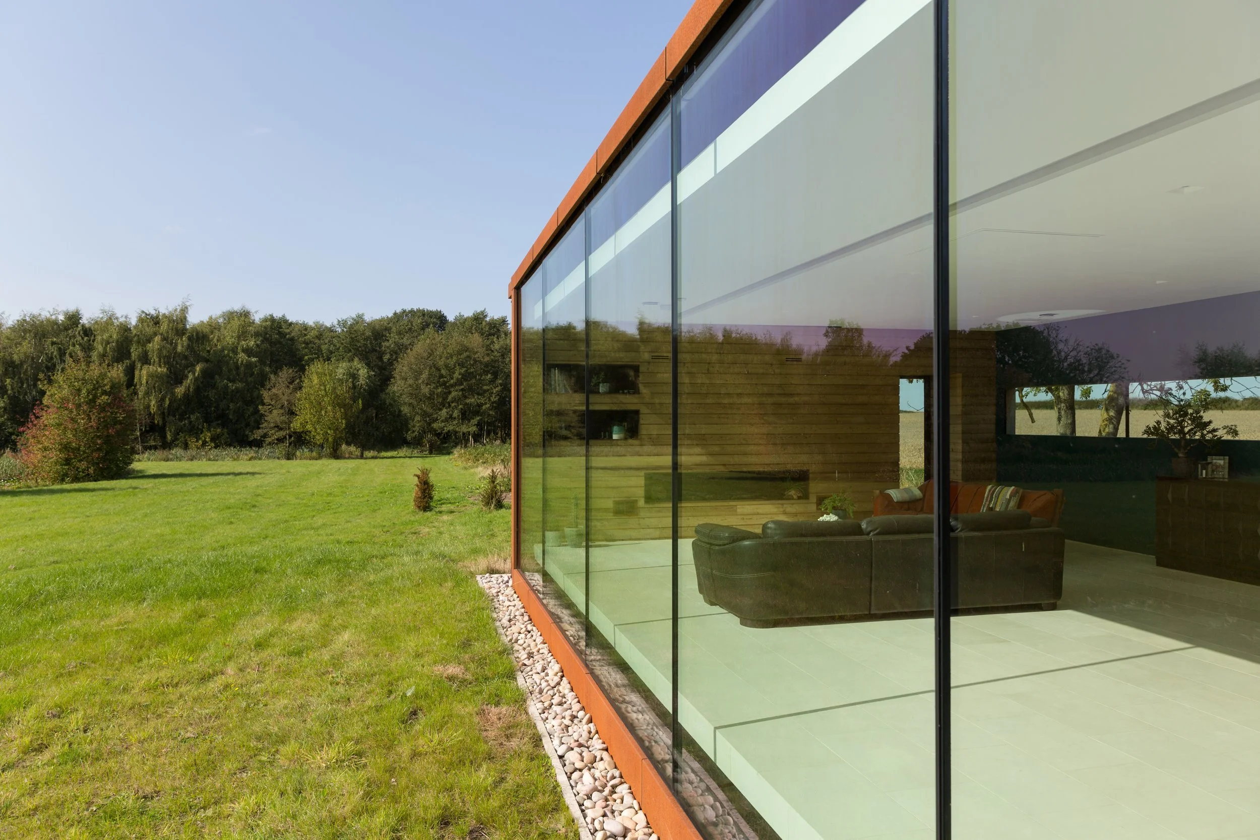 modern eco home with large glass wall looking out over lawn and woodlands beyond
