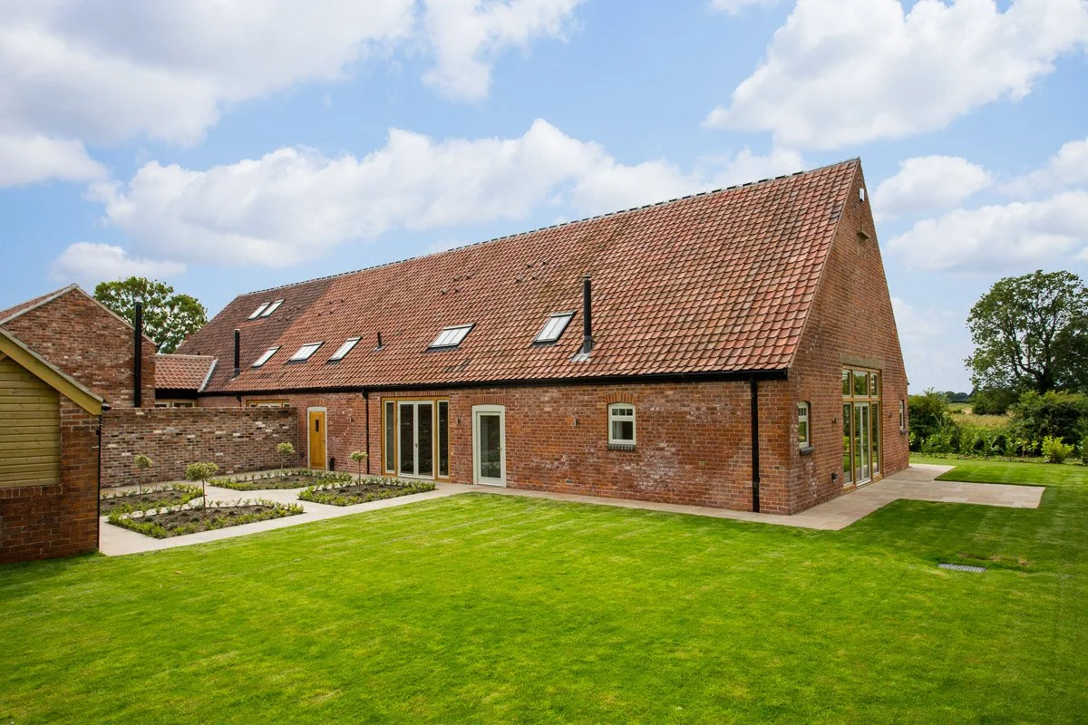 red brick barn conversion with sage green window frames, manicured lawn, vegetable patch 