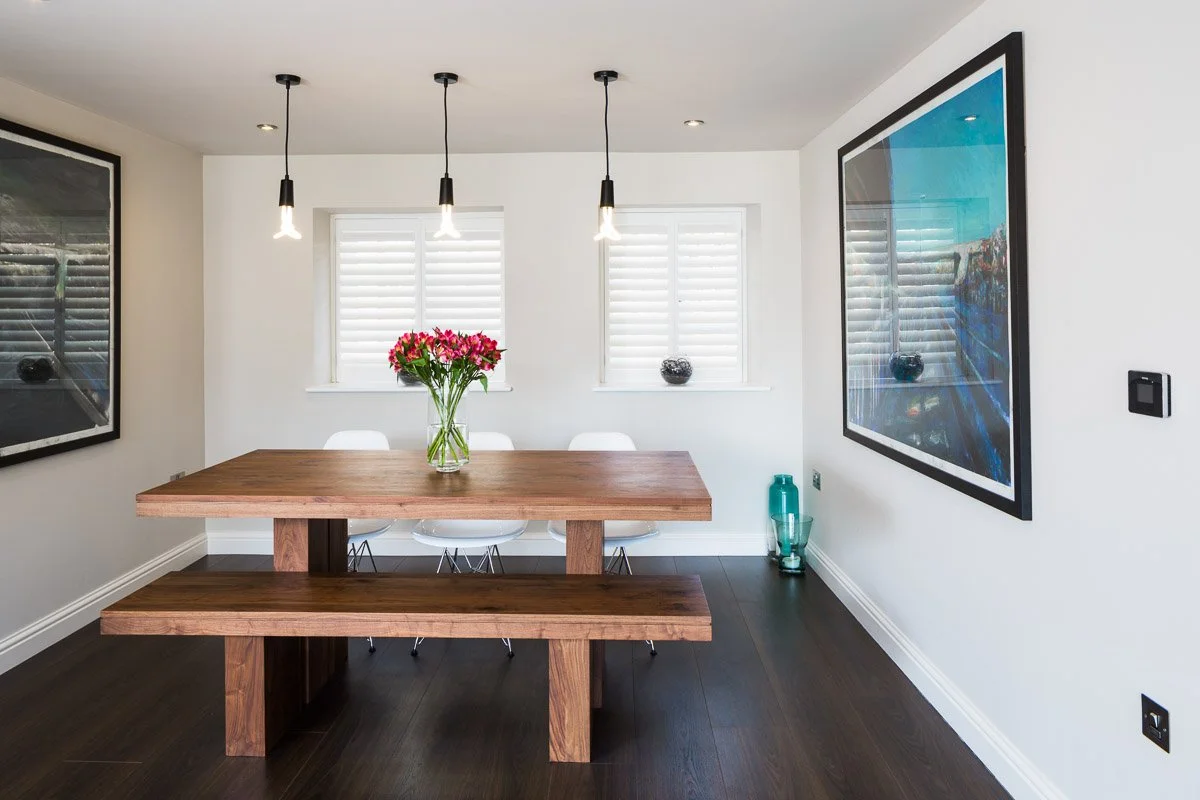 one point perspective of wooden dining table with bench seats and art prints on walls, dark wooden flooring 