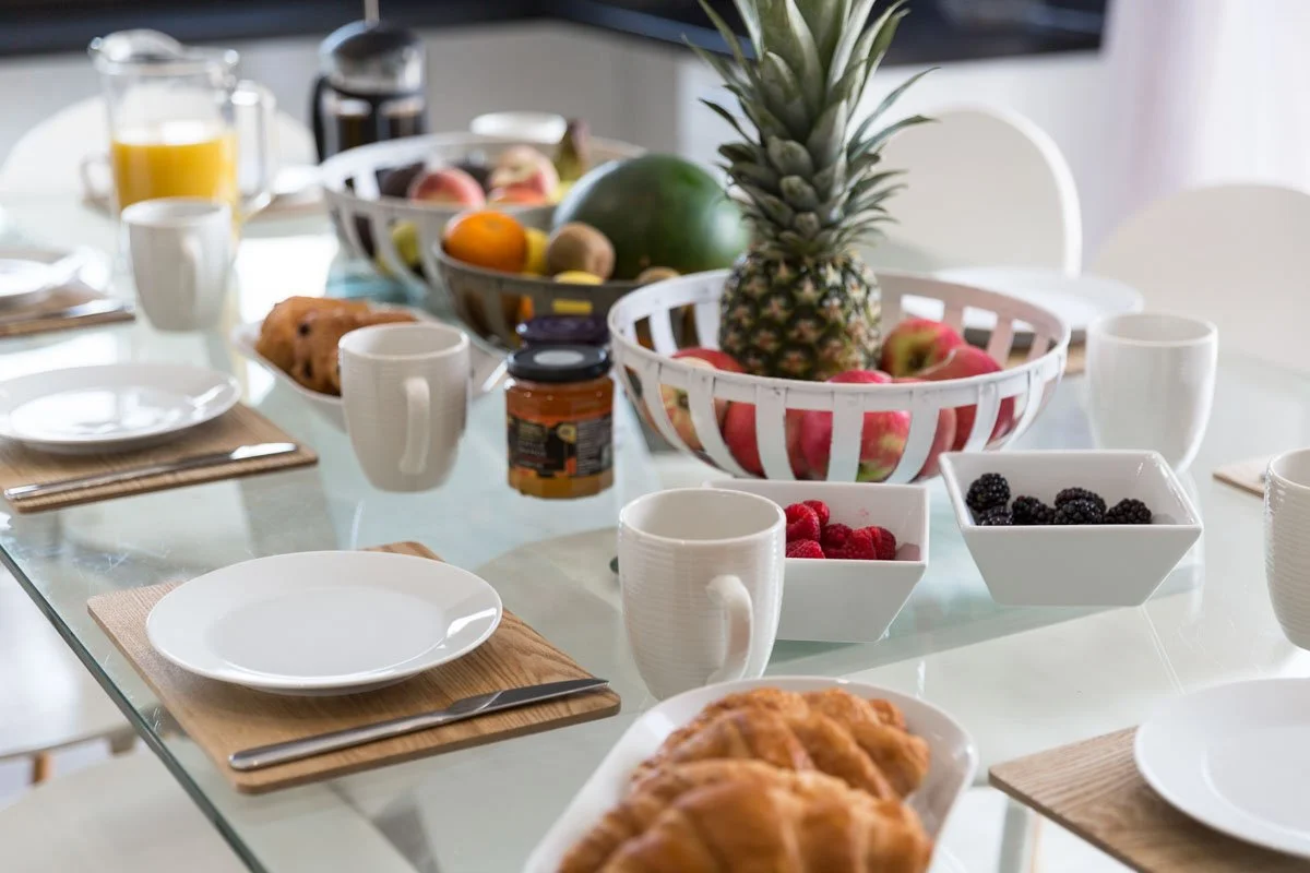 detail image of dining table with plates and cutlery, set up for breakfast with pastries, fruit and coffee