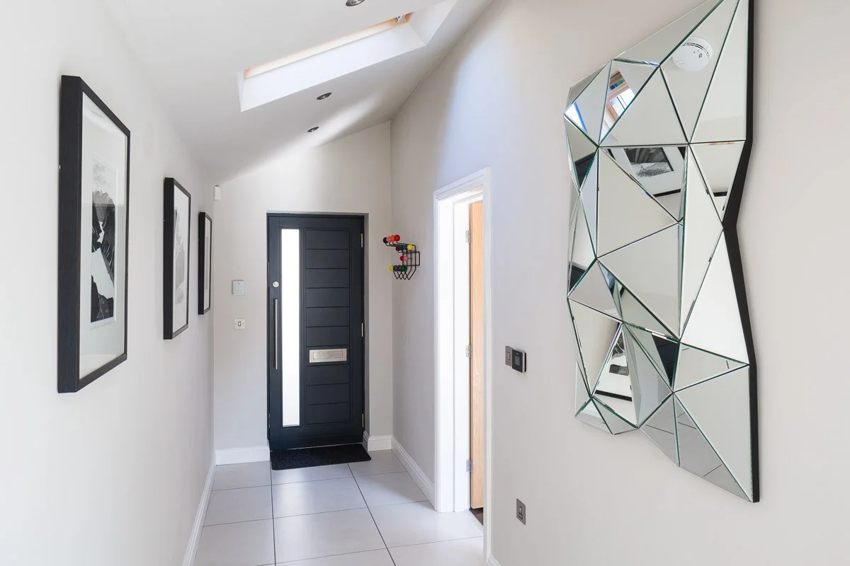 hallway with white walls, wile tile flooring, black modern door and skylight