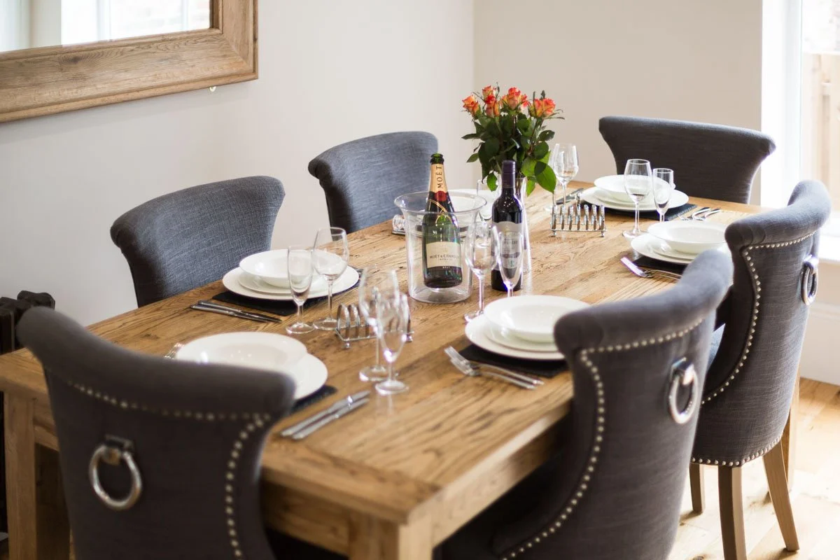 close up of wooden dining table with plates and cutlery, bottle of wine and bottle of champagne sat on table 