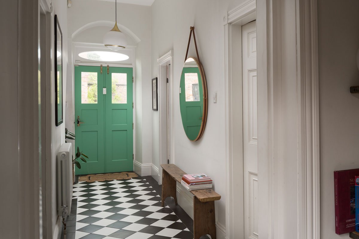 hallway with black and white check flooring, mint green front door, large circular mirror on right hand wall