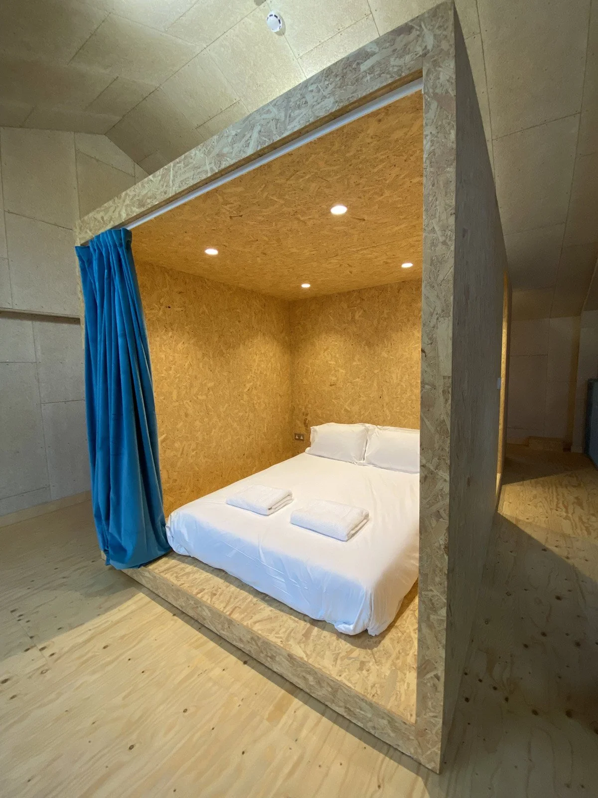 A bedroom with a bed inside a wooden, cube-shaped enclosure with blue curtains on one side.
