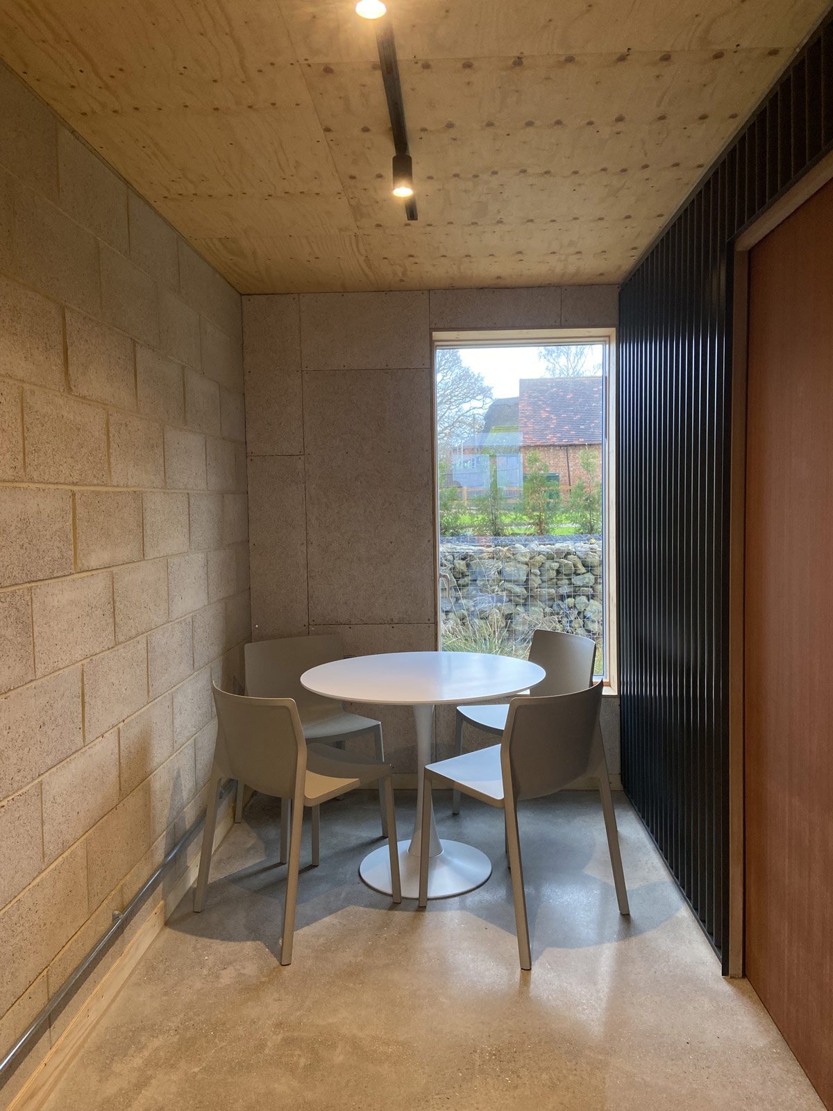Small dining nook with a round white table and four beige chairs, near a large window showing an outdoor scene with rocks and trees.