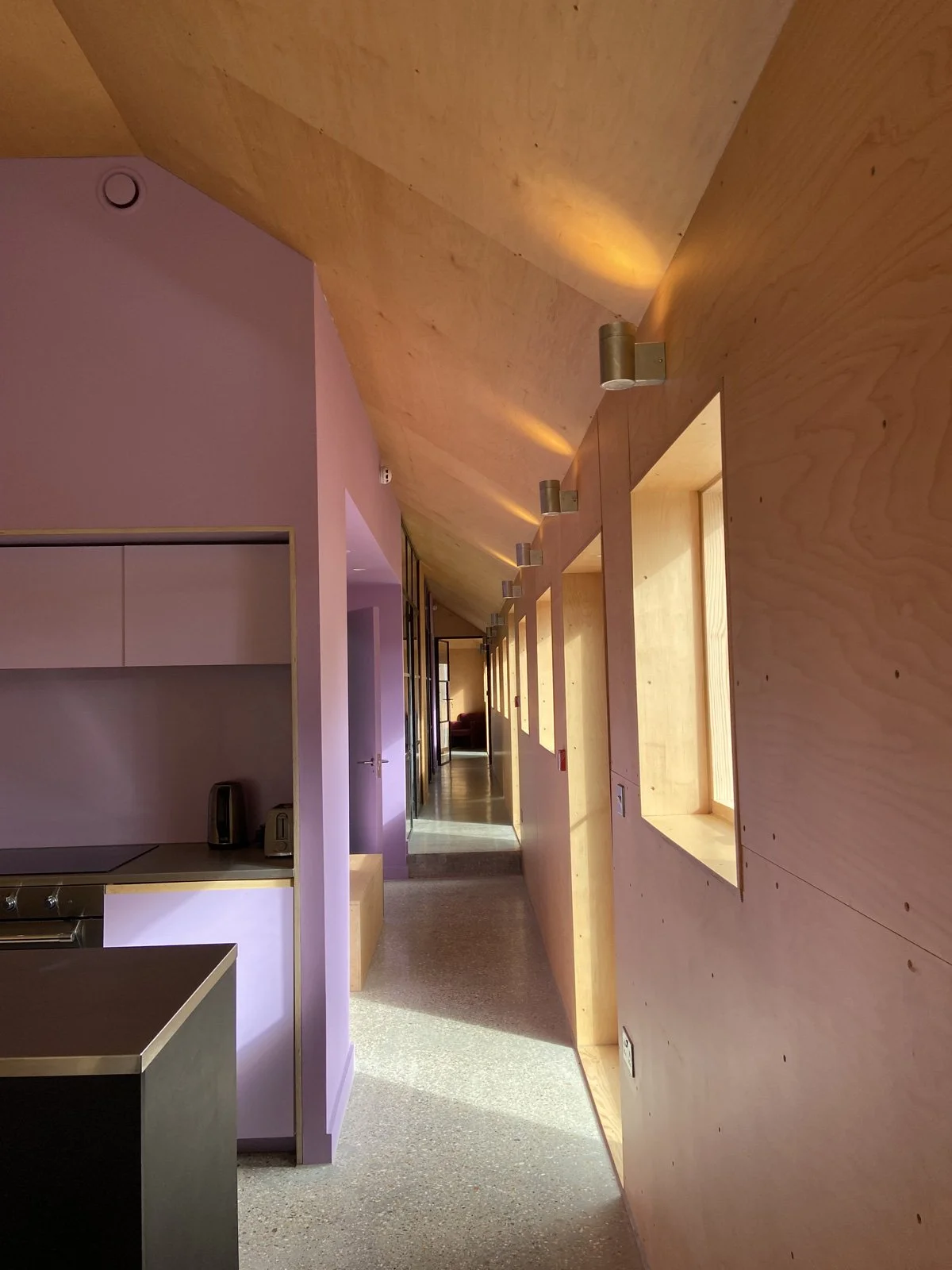 Interior hallway with wooden walls and ceiling, modern wall sconces, and a window allowing natural light.