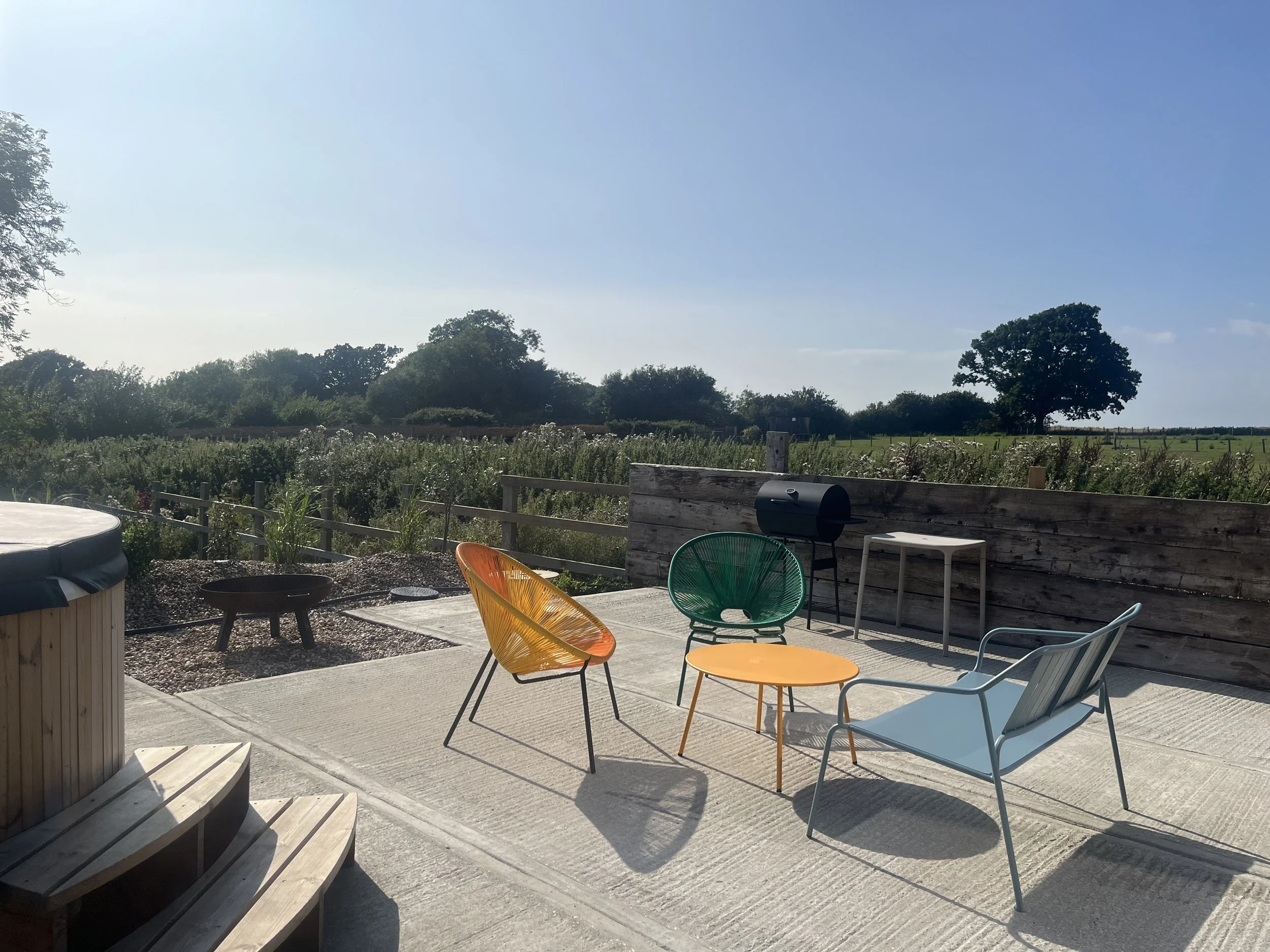 Outdoor patio with colorful chairs, a small table, and a distant view of fields and trees on a sunny day.