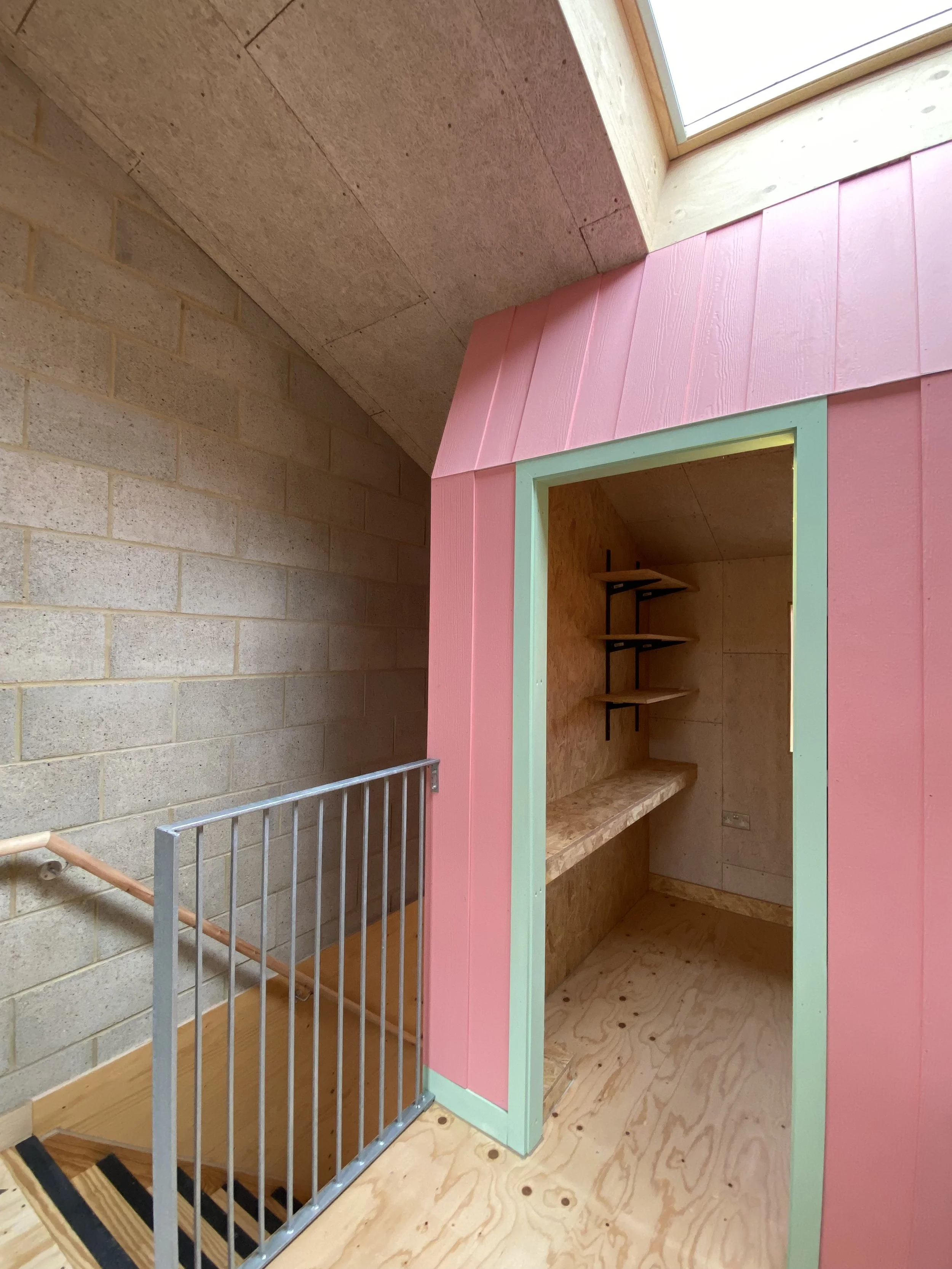 Interior of a small colorful wooden playhouse with pink exterior walls, mint green doorframe, inside shelves, and a plywood interior.