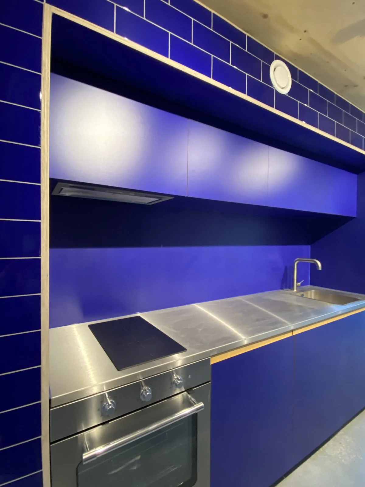 Modern kitchen with a blue tiled wall, stainless steel countertop, stove, and sink.