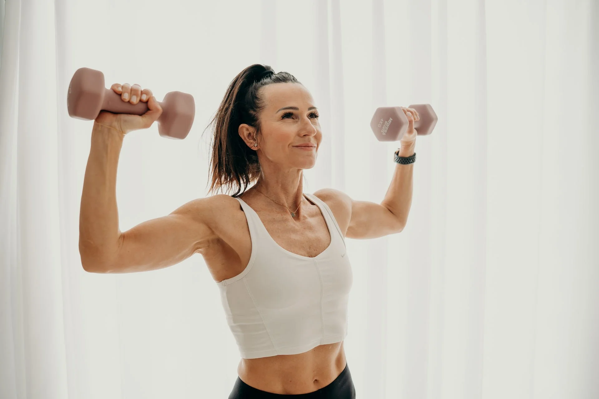 Frau macht Krafttraining mit Hanteln in hell ausgeleuchteter Räumlichkeit.