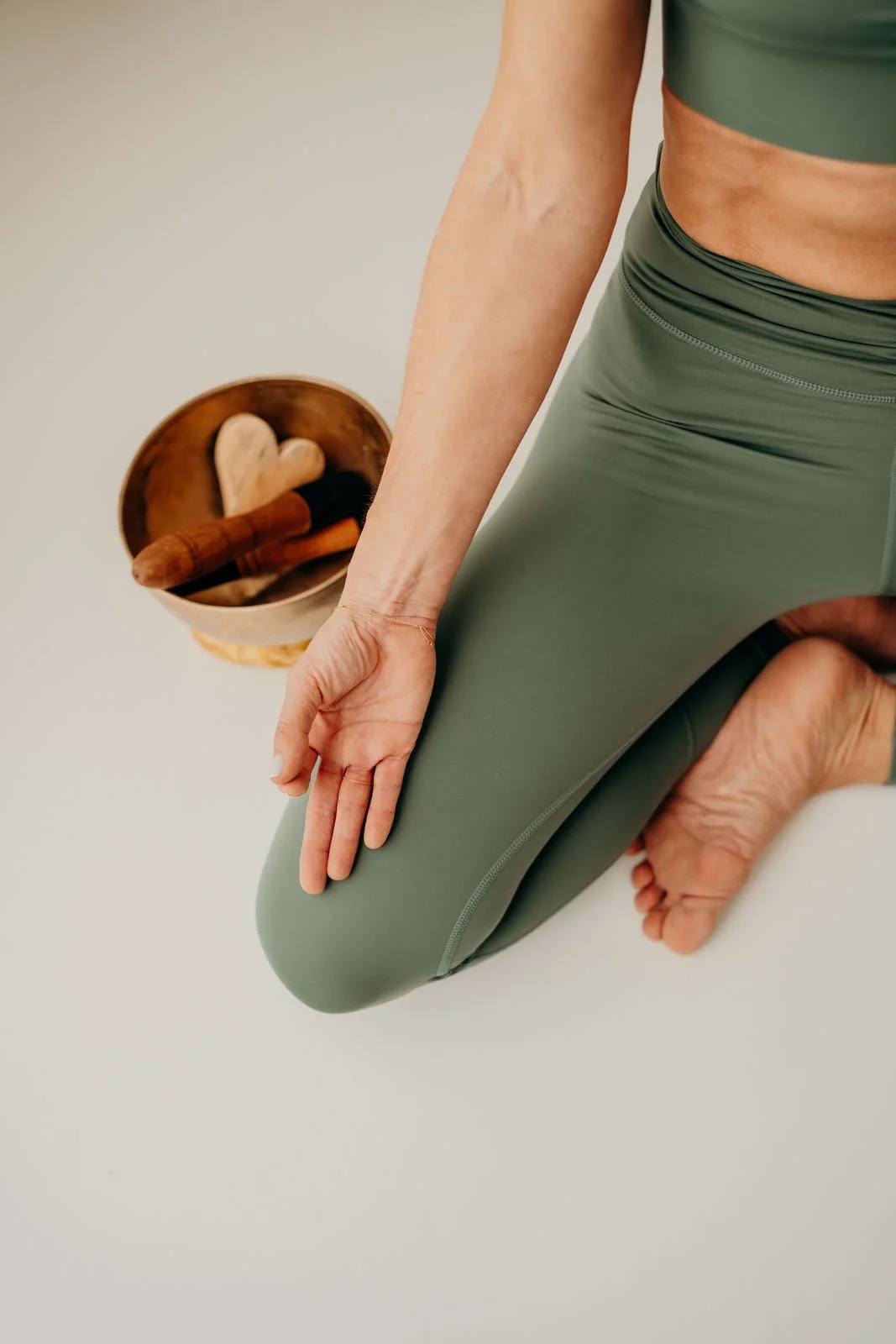 Ein Mensch in grüner Yogahose macht eine Yoga-Pose auf einem weißen Boden, neben einem Holzschale mit Massagewerkzeugen.