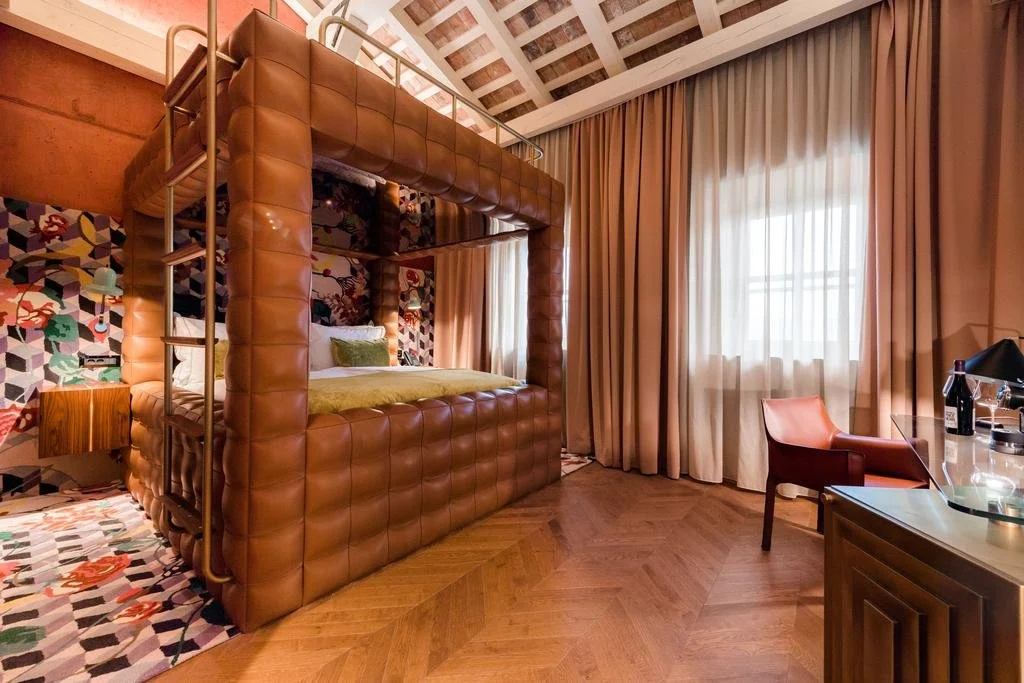 Ein Schlafzimmer mit einem Bettturm, bunten Wandtapete mit Tiermotiven, Vorhängen und einem Schreibtisch mit Lampe belastet.