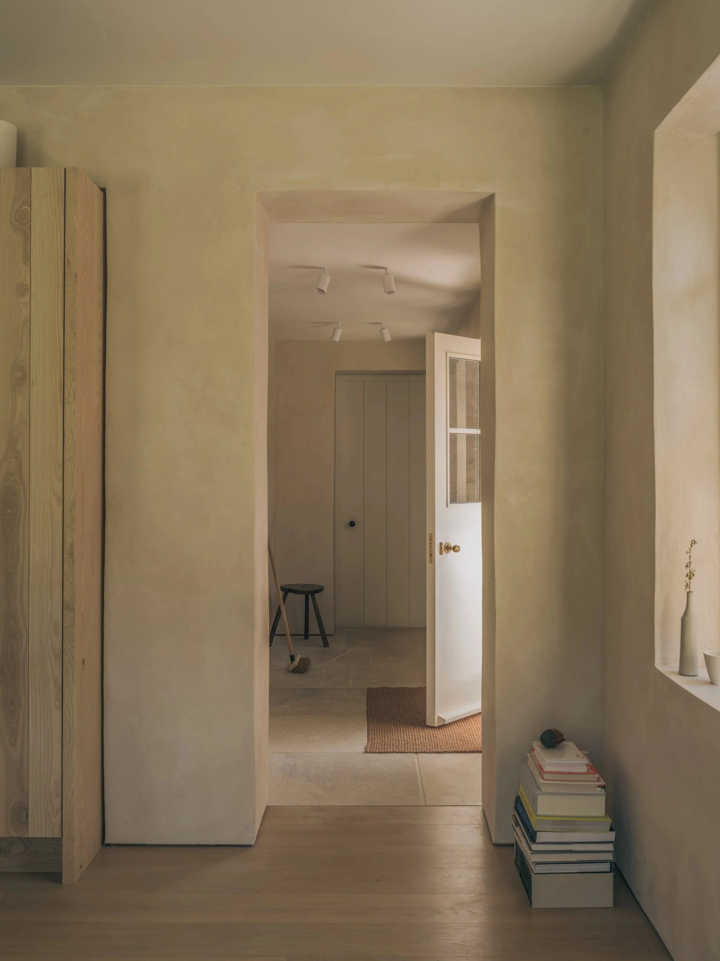 Interior view of a doorway leading to a room with storage closet, a broom leaning against the wall, and a stack of books on the floor.