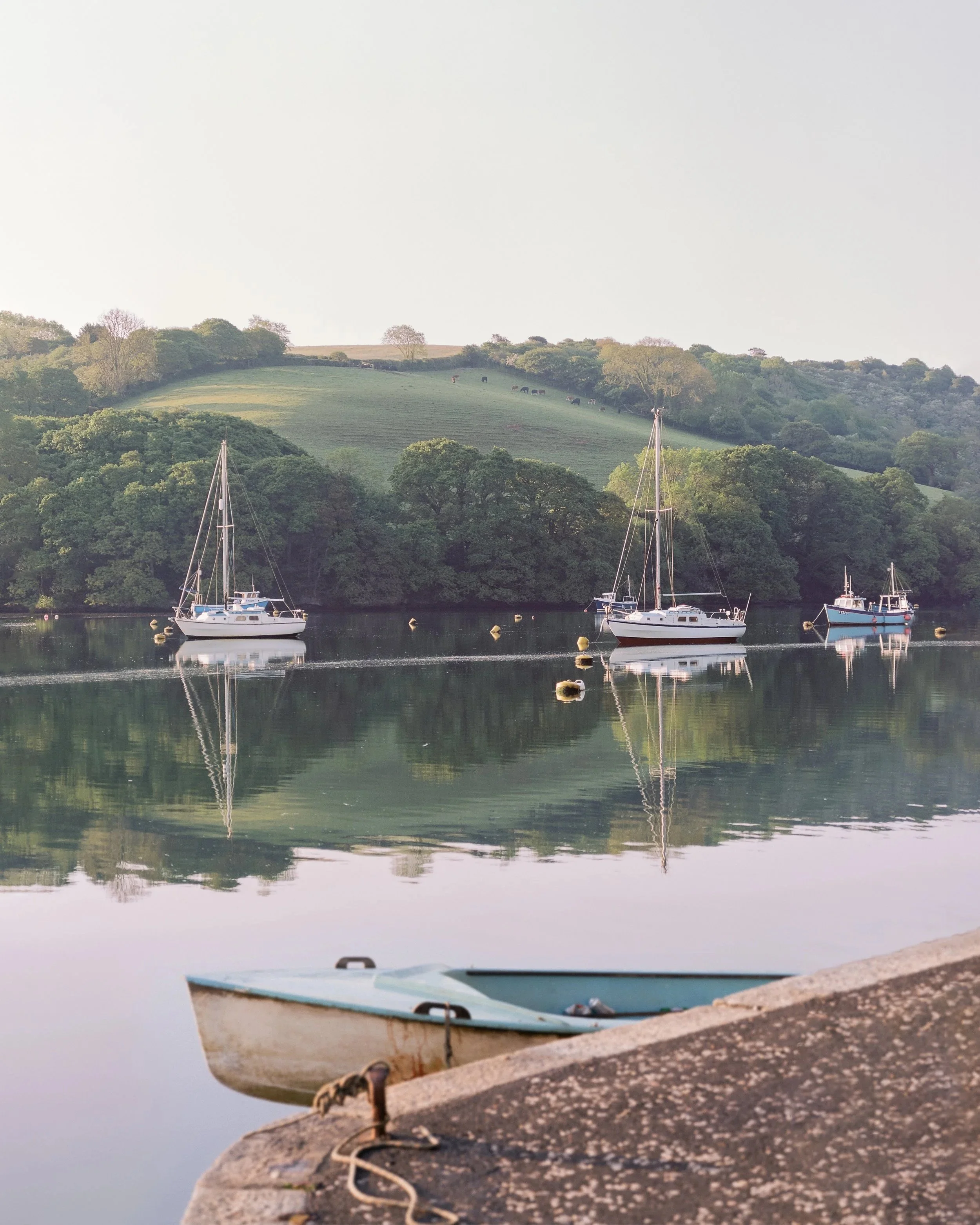 Boats docked along a river with green hills and trees in the background.