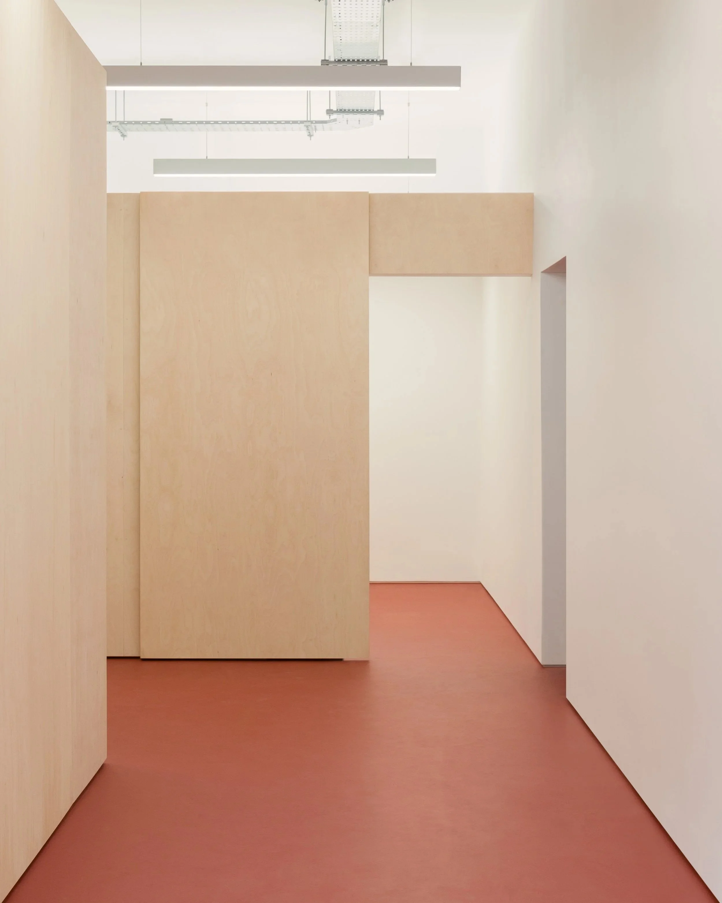 Minimalist interior space with beige walls and a reddish-brown floor, featuring crane-like ceiling fixtures.