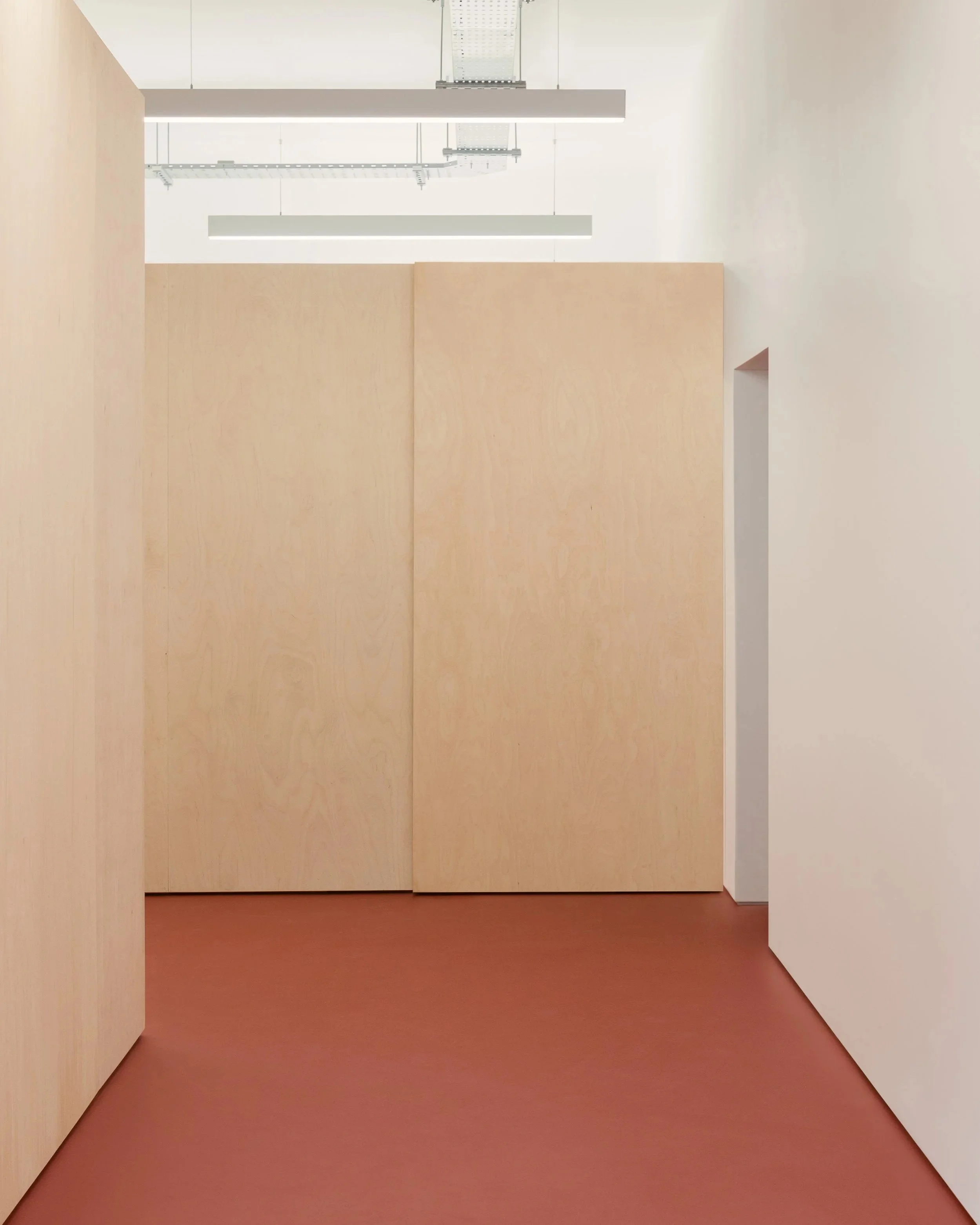 Minimalist interior with beige and white walls, brown floor, and suspended ceiling lights.