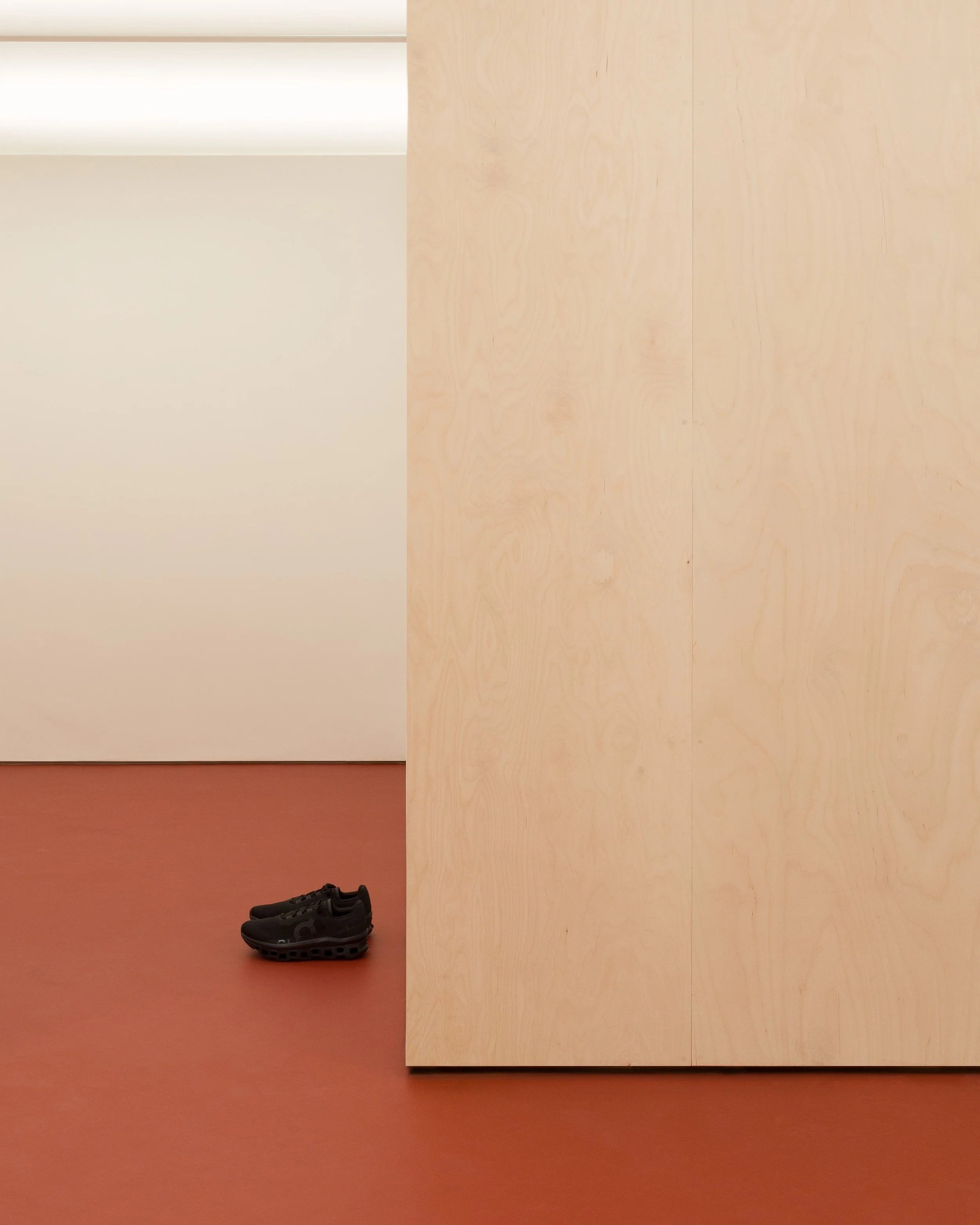 Pair of black sneakers on a reddish-brown floor with wooden wall panels in the background.