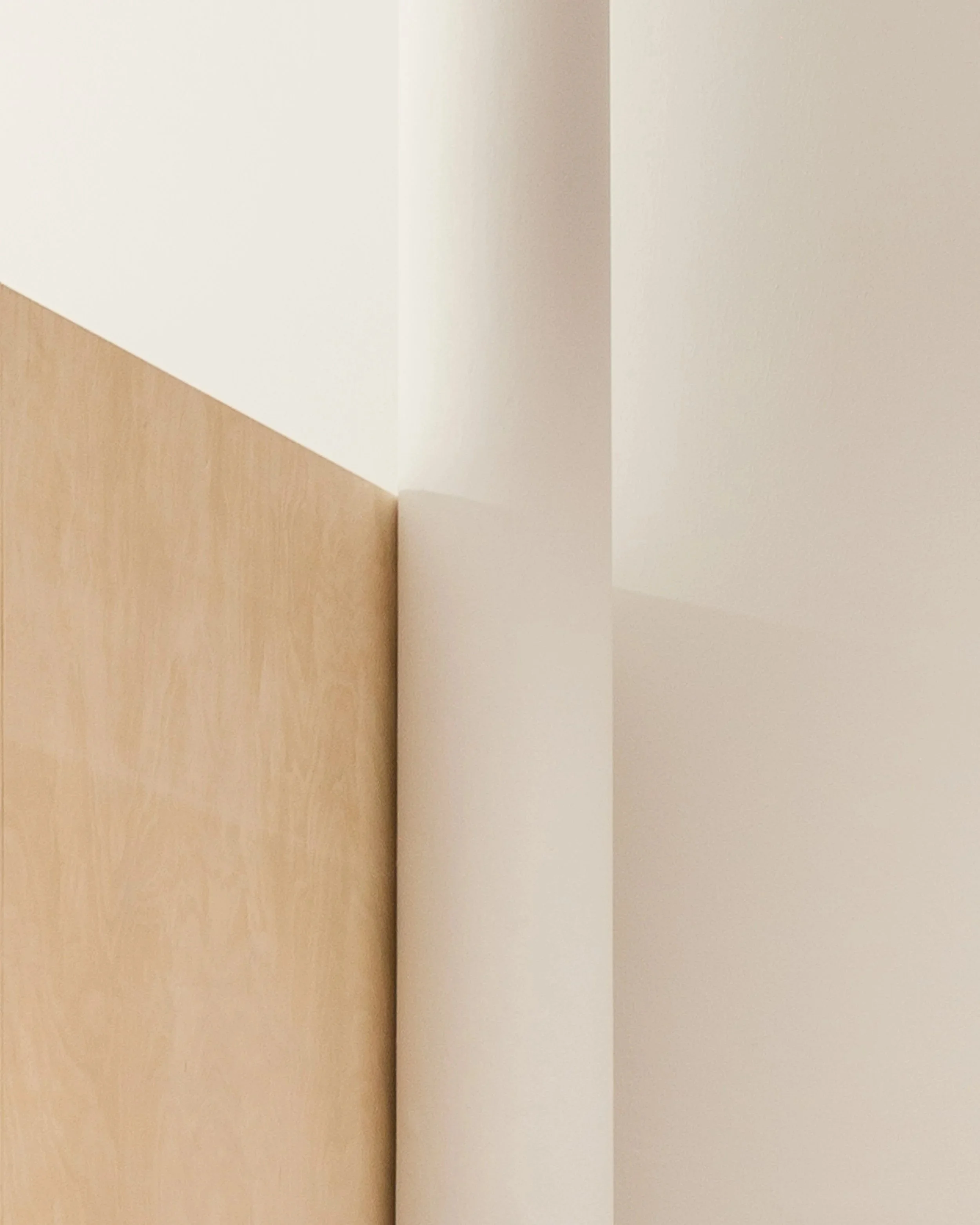 A corner of a room showing white and beige walls with a wooden floor.