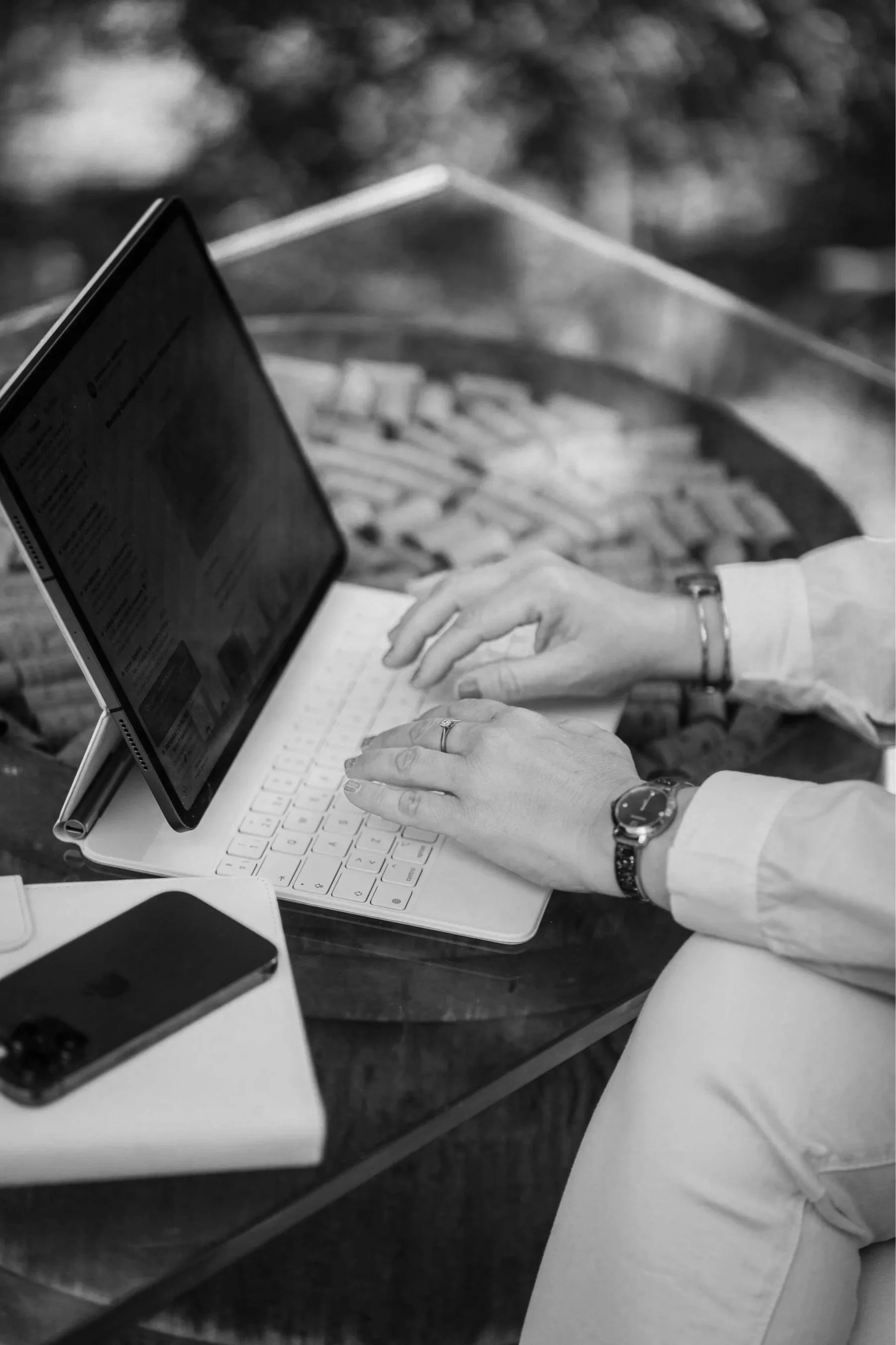 Nahaufnahme eines Laptops, mit Hochzeitsplanerin Alexandra, die darauf tippt, auf einem Schreibtisch. Im Hintergrund sind andere Gegenstände sichtbar, darunter ein Smartphone und ein Tablet.