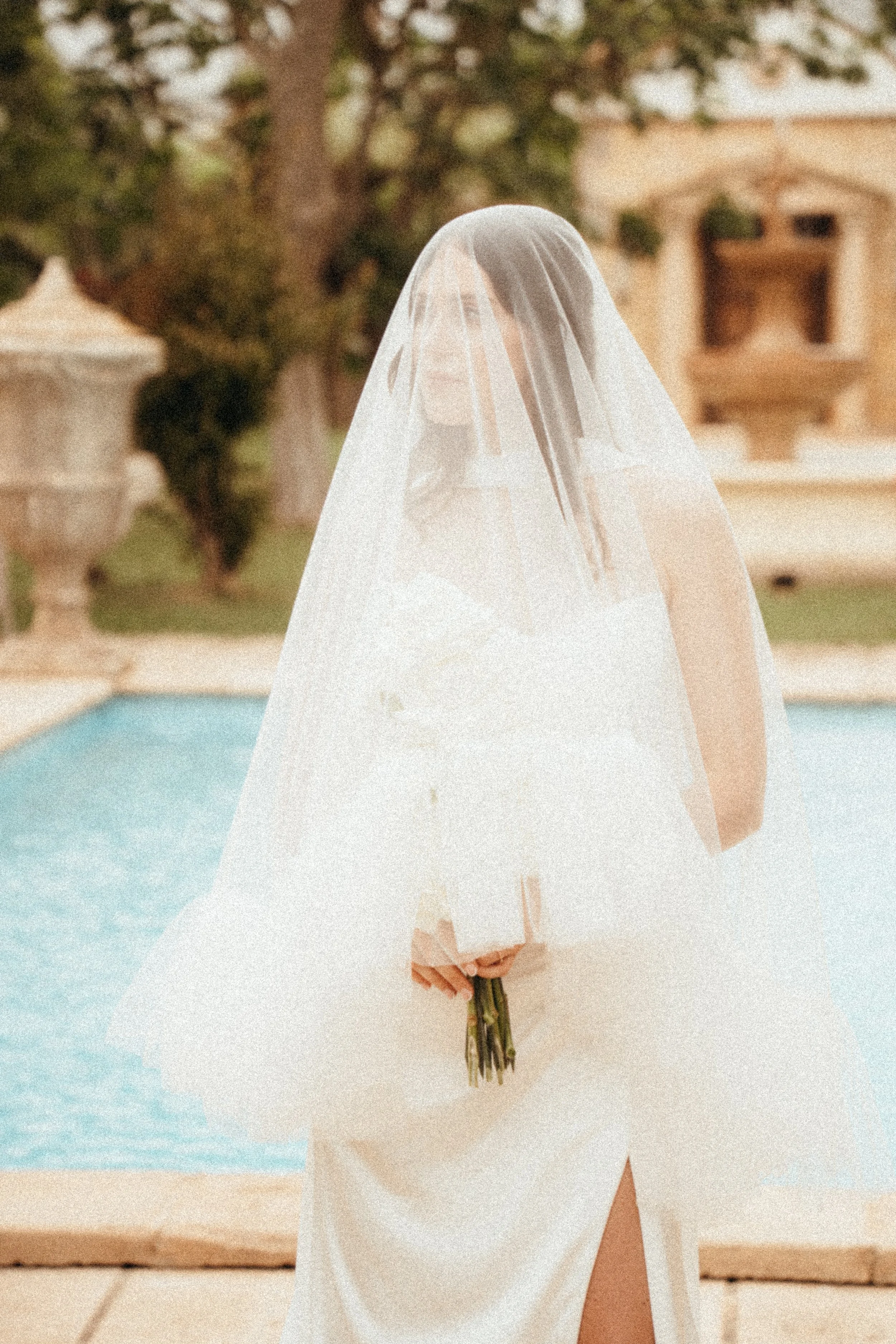 Frau in Hochzeitskleid mit Schleier hält einen Blumenstrauß bei einer Hochzeit am Pool