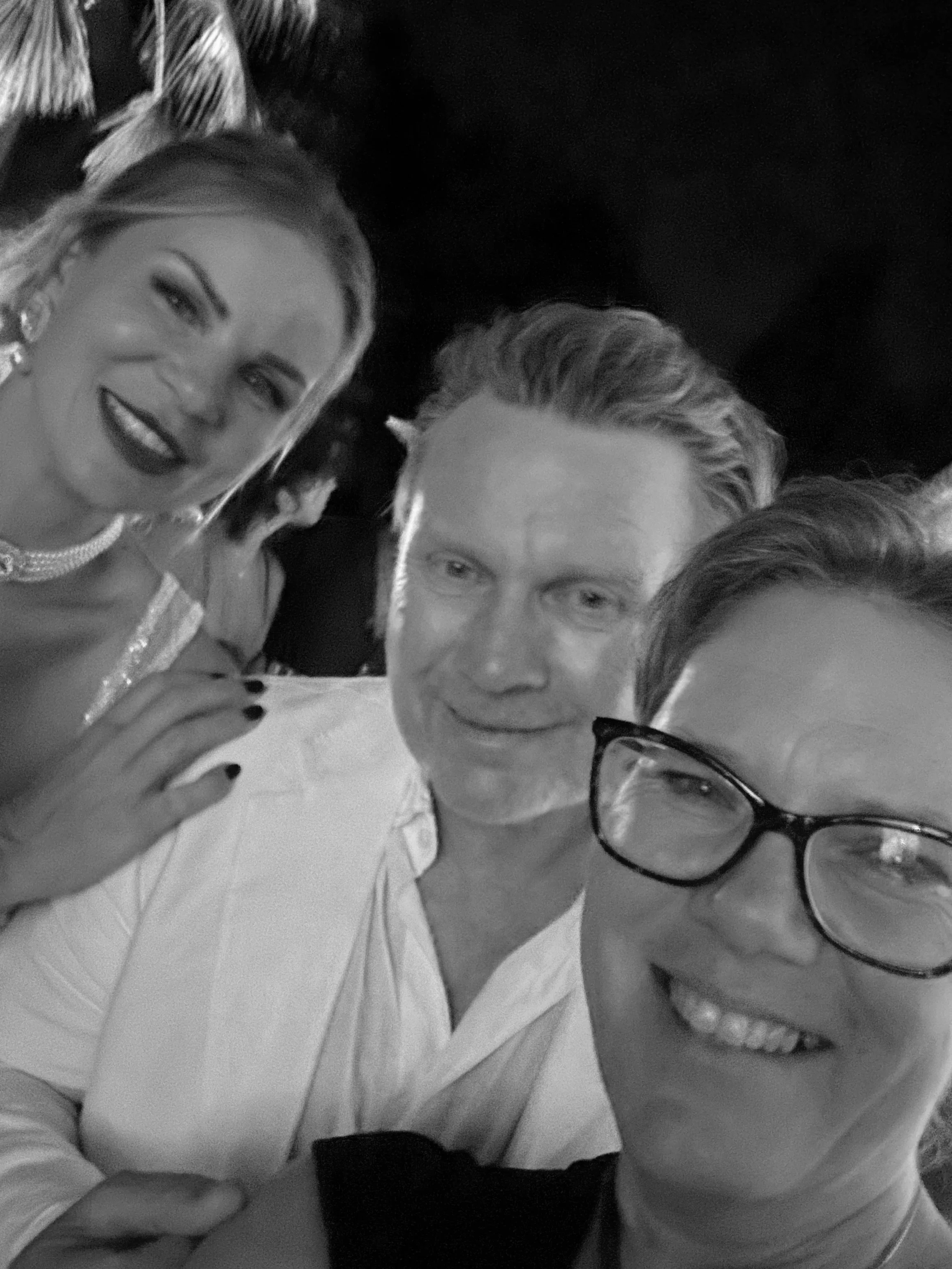 Alexandra mit ihrem Brautpaar, Nahaufnahme einer Gruppe von Menschen, die sich für ein Foto versammeln, lächelnd und in formellen Kleidung, einige tragen Brillen und Schmuck, im Schwarz-Weiß-Stil aufgenommen.