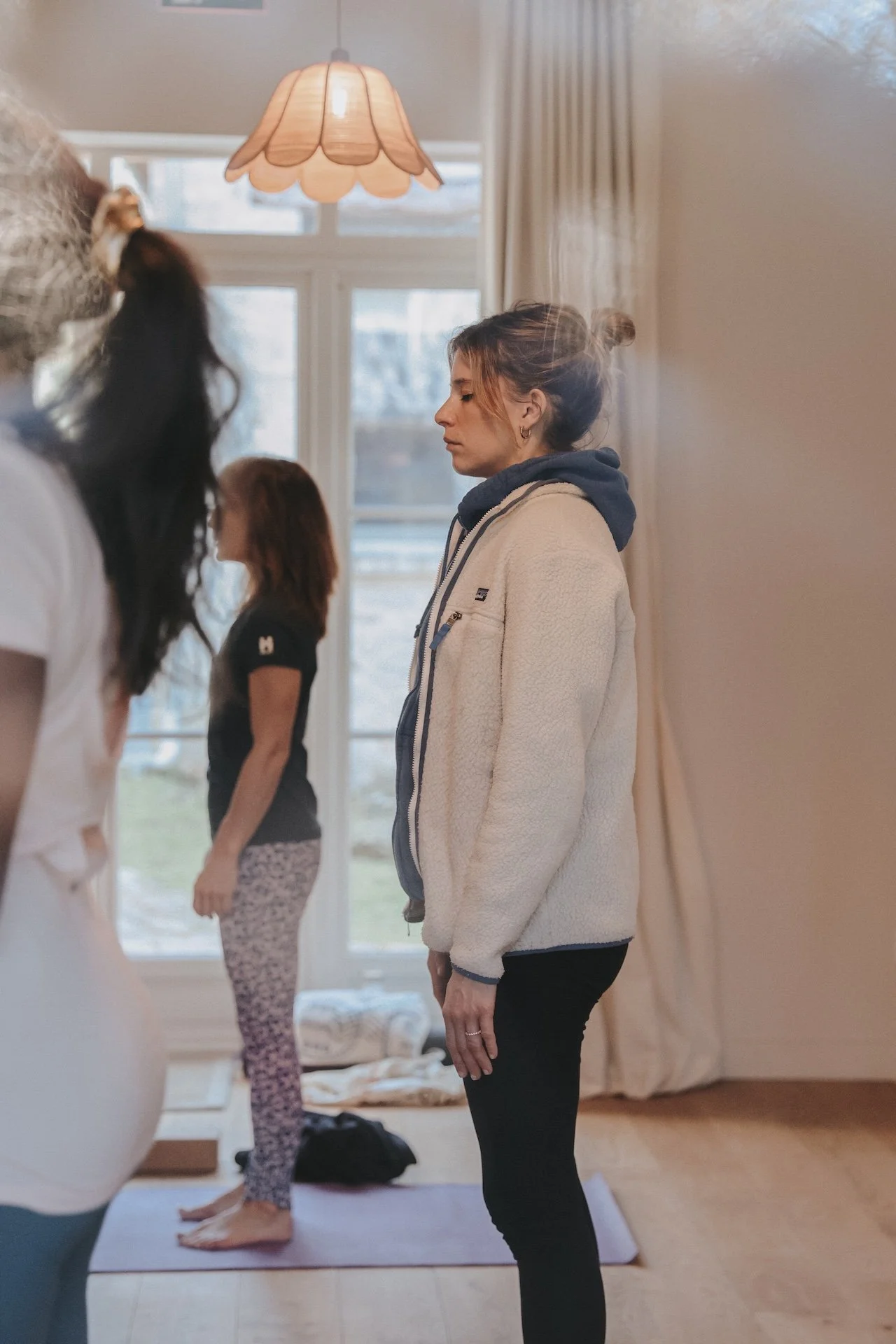 Trois participantes en tadasana de profil dans une salle lumineuse donnant sur le jardin — retraite de yoga en pleine nature, Baie de Somme