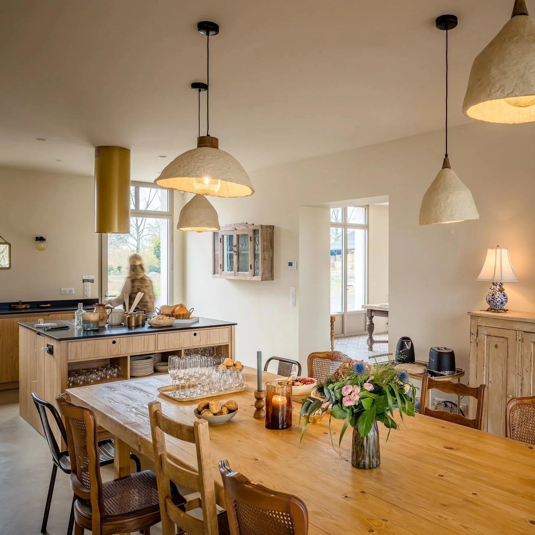 Salle à manger lumineuse avec cuisine ouverte en arrière-plan et silhouette d'une participante en mouvement — la vie douce lors d'un voyage célibataire à la campagne