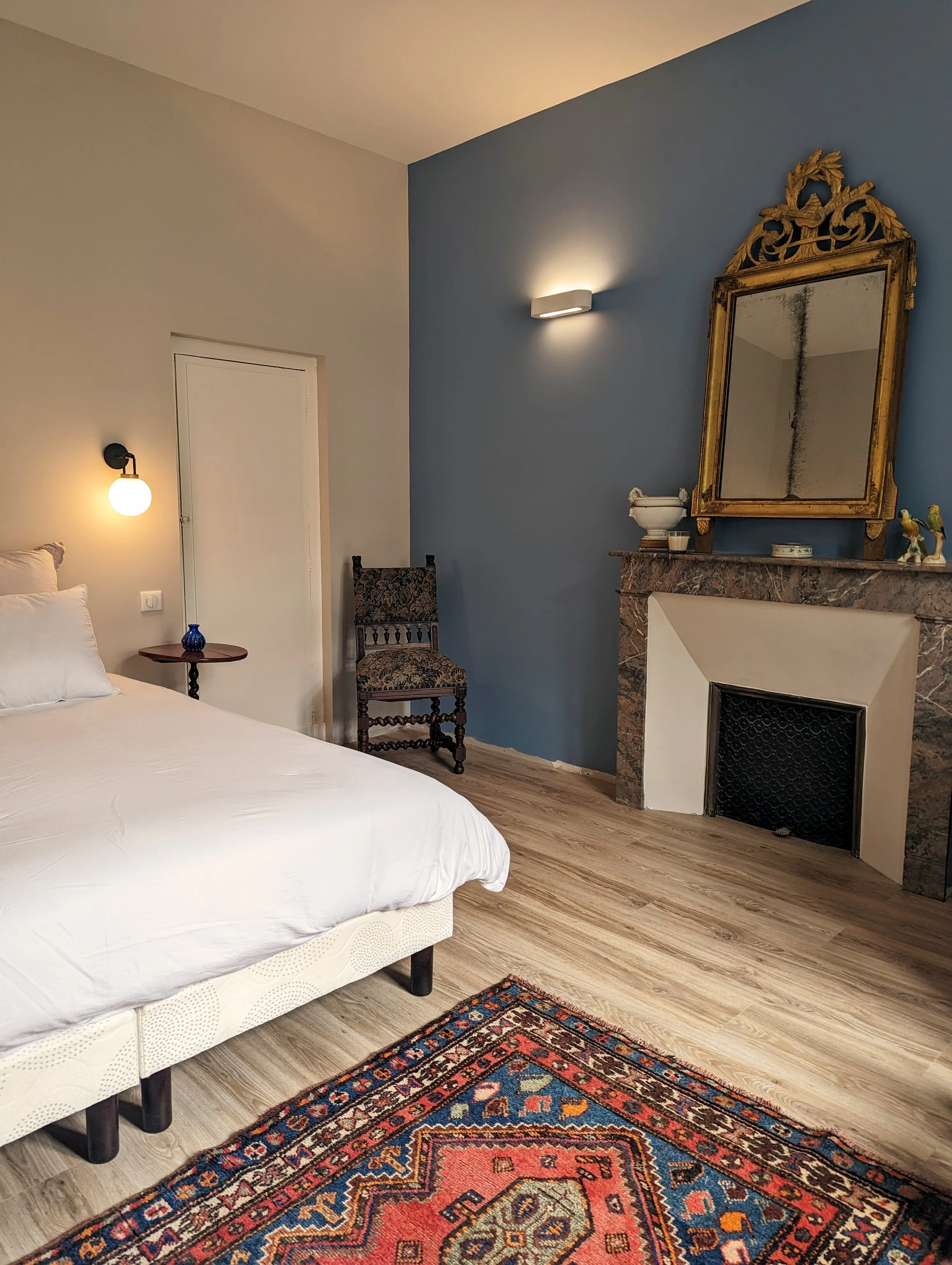 Chambre lumineuse et chaleureuse avec lit double, cheminée ancienne et miroir doré, idéale pour un séjour ressourçant en pleine nature dans l’Aude.