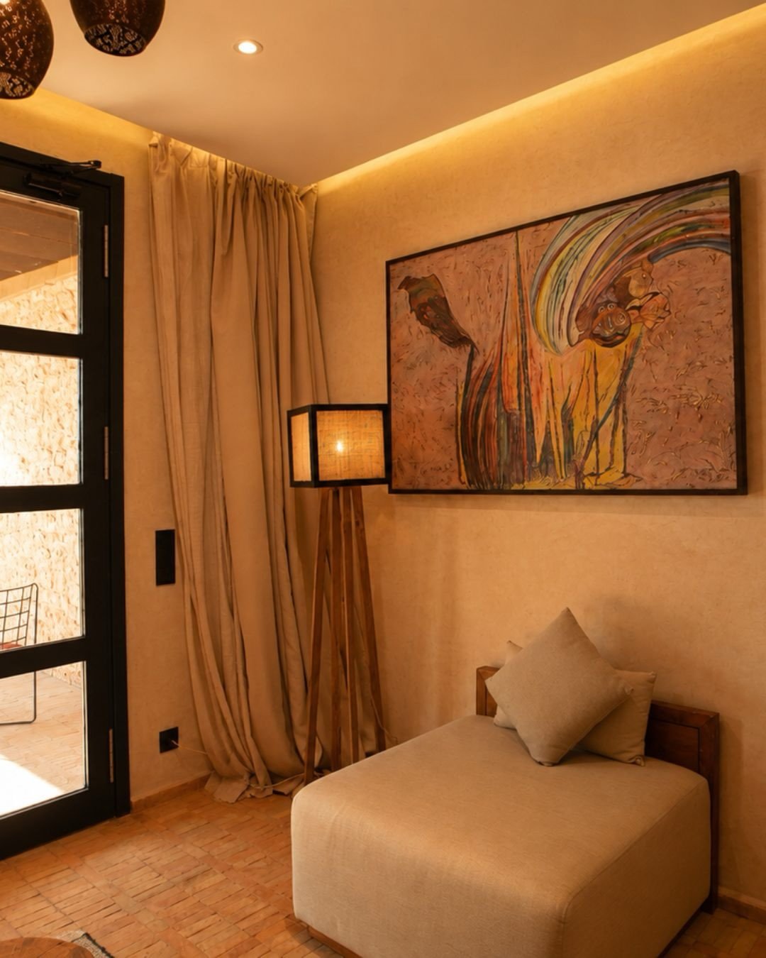 Salon de chambre avec canapé, lampe en rotin et tableau africain — suite premium retraite yoga équitation Essaouira Maroc