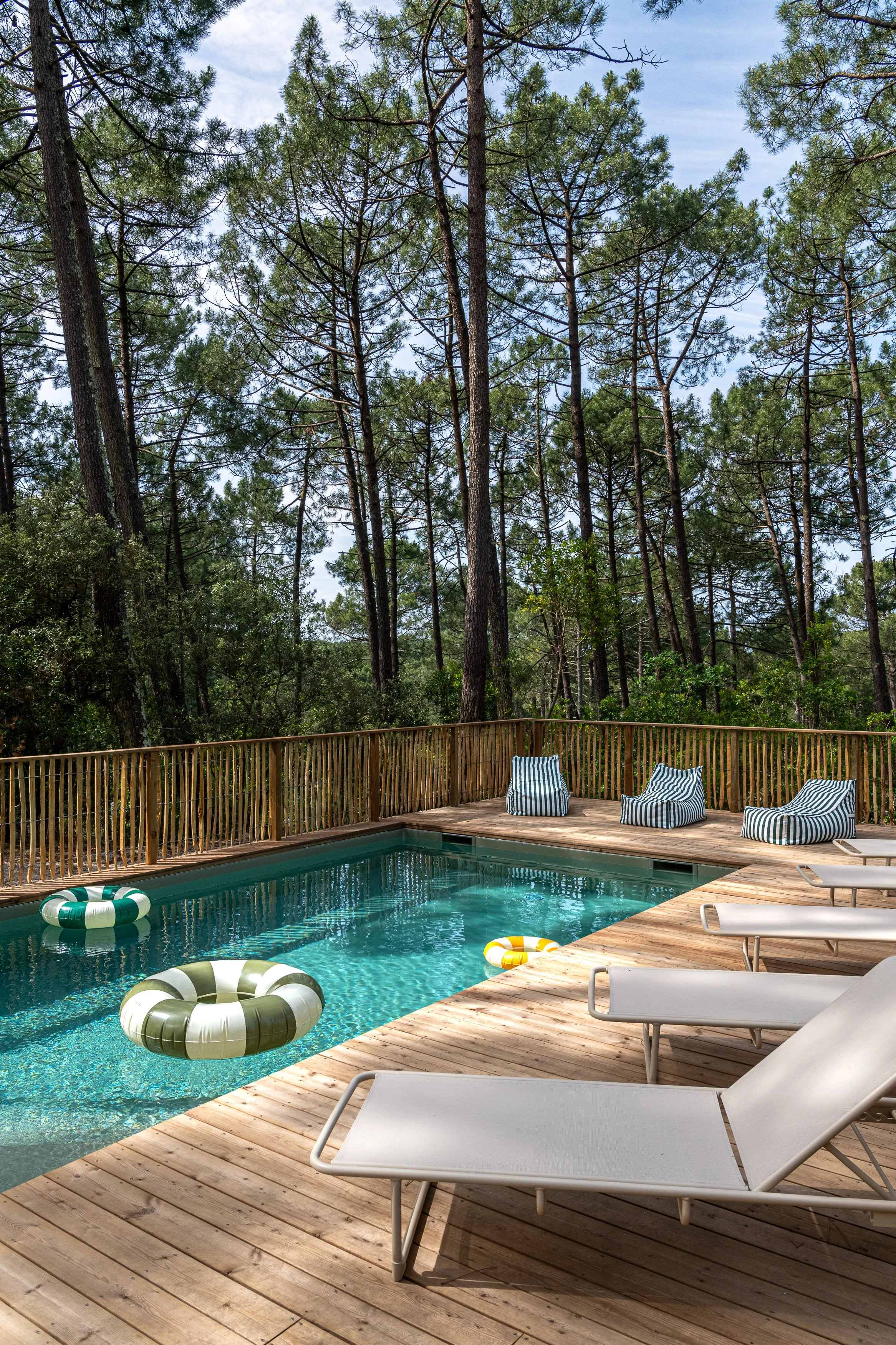 Piscine extérieure entourée de pins et de transats rayés, parfaite pour se détendre après une journée de yoga et de surf sur la côte Atlantique.