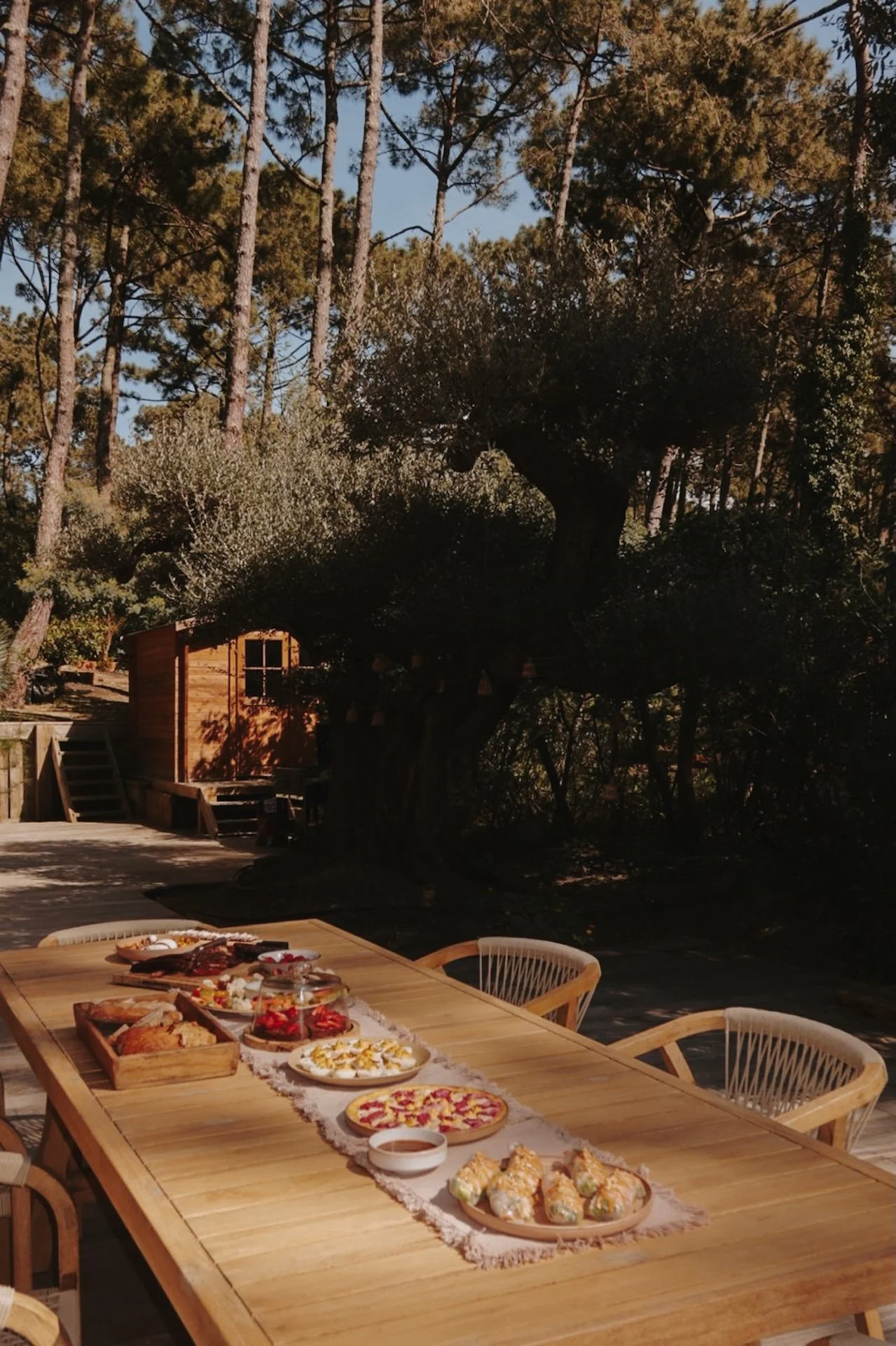 Table dressée en extérieur sous les pins à la tombée du jour — repas conviviaux d'une retraite yoga bord de mer dans les Landes