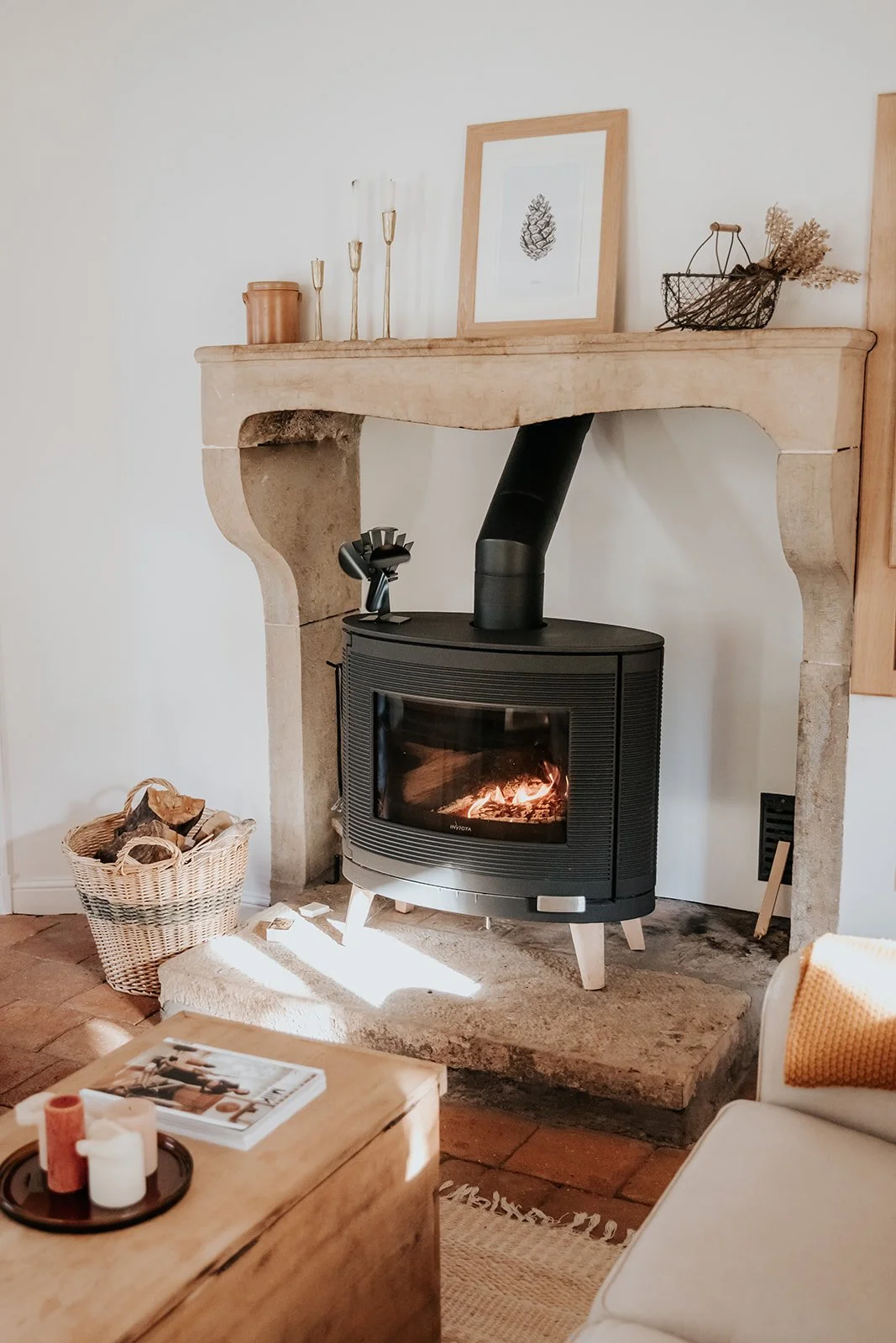 Cheminée en pierre sculptée avec poêle à bois allumé — ambiance cocooning vacances automne France retraite bien-être