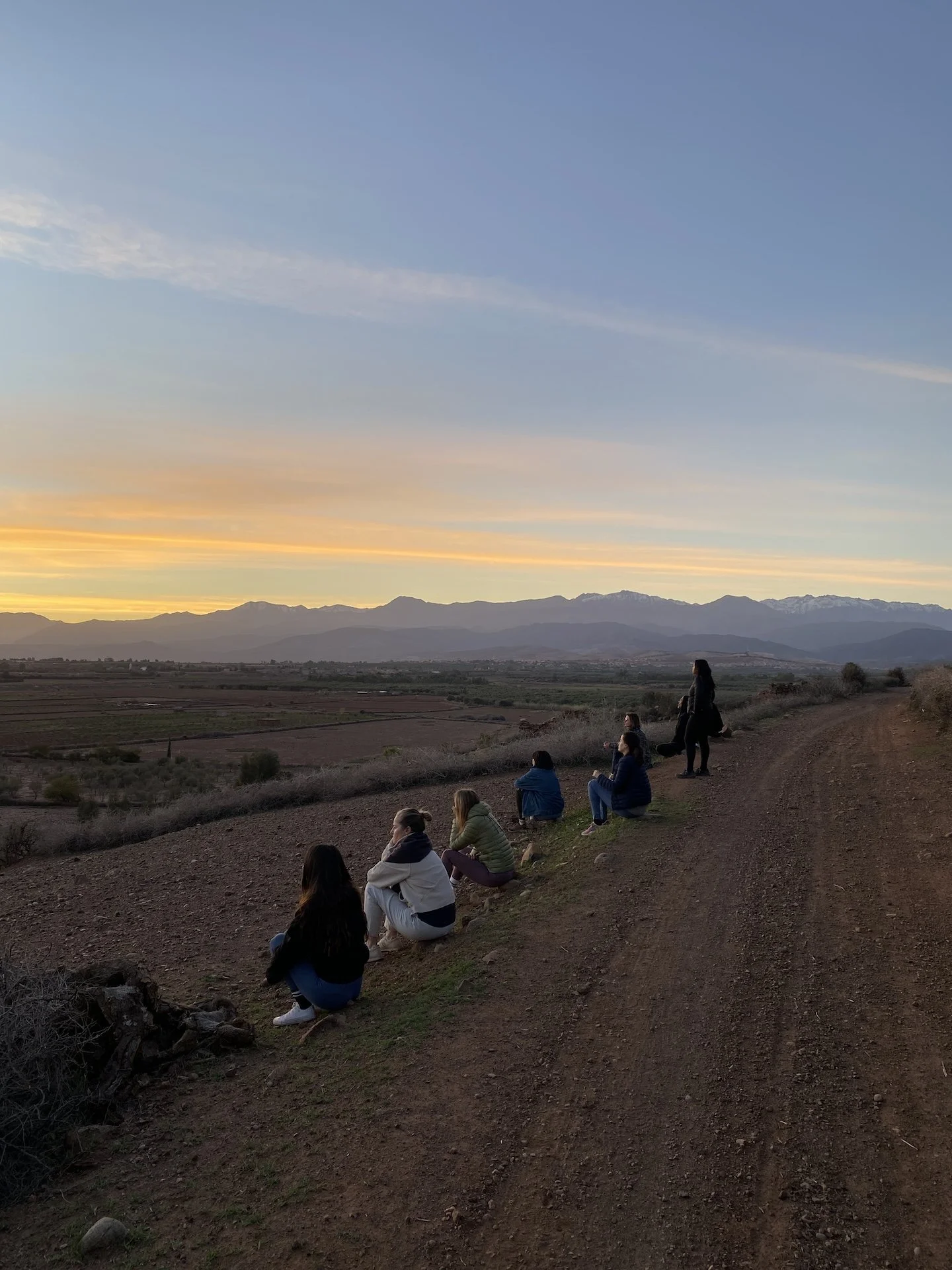 Groupe de femmes contemplant le coucher de soleil face à l'Atlas — retraite yoga arrière-pays Marrakech novembre 2026