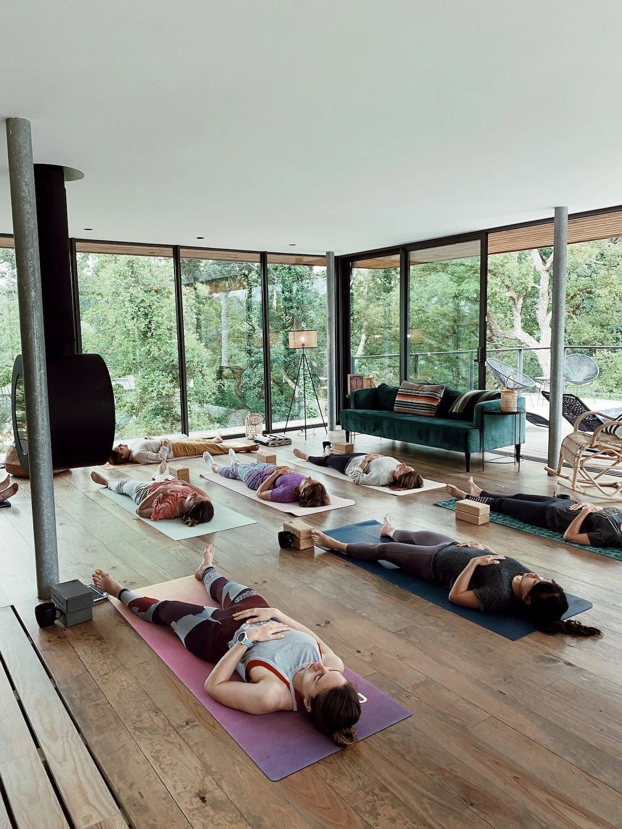 Groupe en savasana lors d'un cours de yoga collectif dans une salle avec baies vitrées sur la forêt, retraite bien-être nouvel an Landes