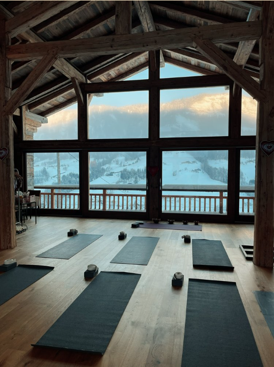 Une salle de yoga ou de méditation avec des tapis et des blocs de yoga, ayant une grande fenêtre donnant sur des montagnes enneigées pour une retraite de yoga d'exception dans les Alpes