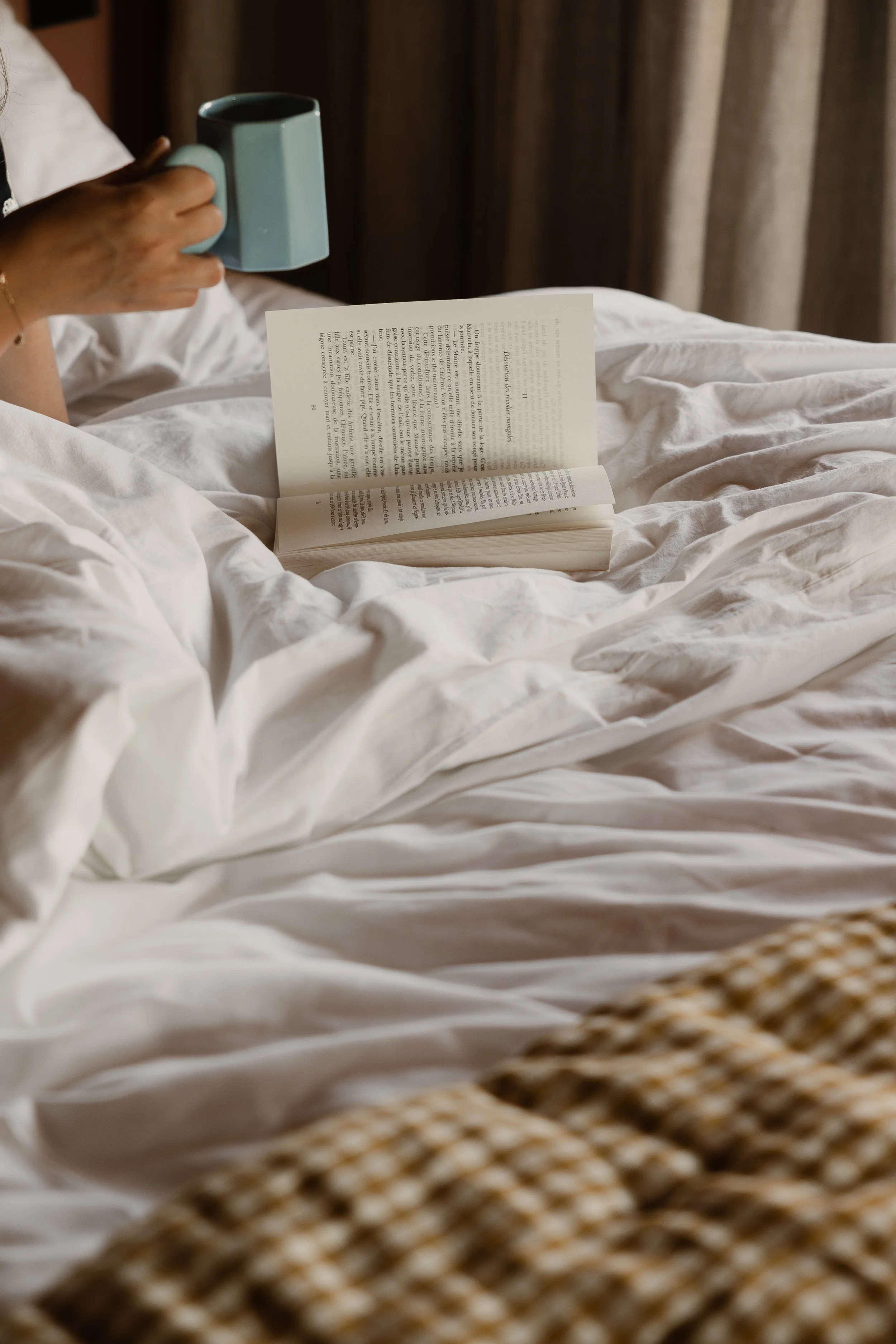 Moment cocooning avec une tasse chaude au lit. Une atmosphère feutrée et raffinée, symbole du confort exclusif de cette retraite yoga premium.