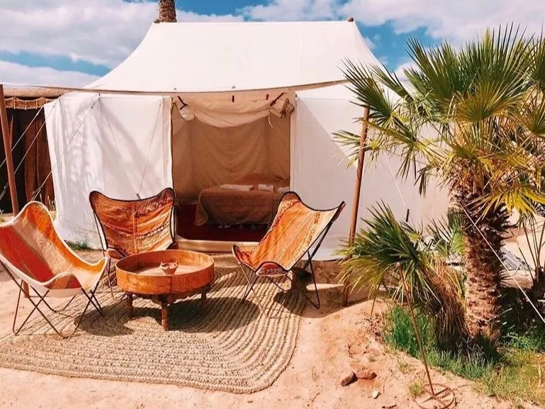 Tente safari avec fauteuils en cuir et palmier dans le désert d'Agafay — glamping retraite yoga Marrakech Maroc 2026