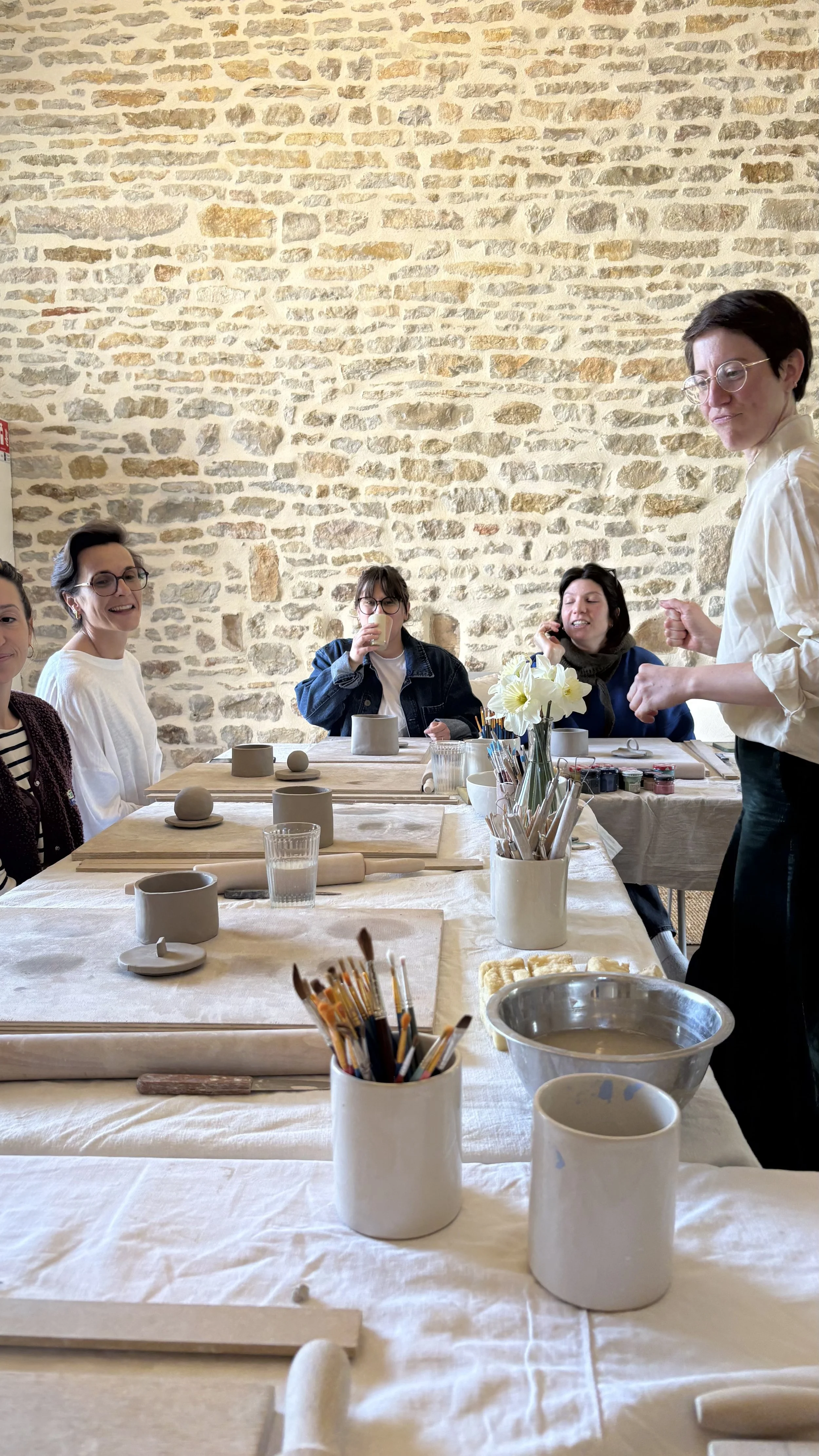 Groupe de femmes souriantes autour d'une table d'atelier céramique, murs en pierres apparentes — retraite yoga créative et holistique Bourgogne automne