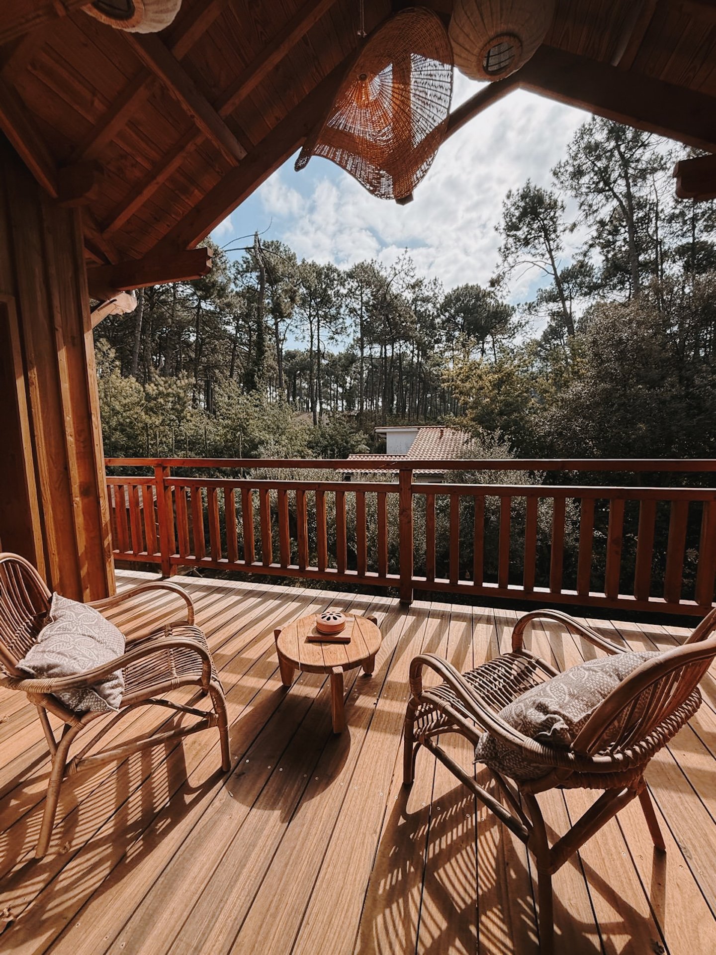 Terrasse en bois et fauteuils en rotin sous les pins, vue sur la forêt landaise — moment de détente dans une retraite yoga Sud-Ouest
