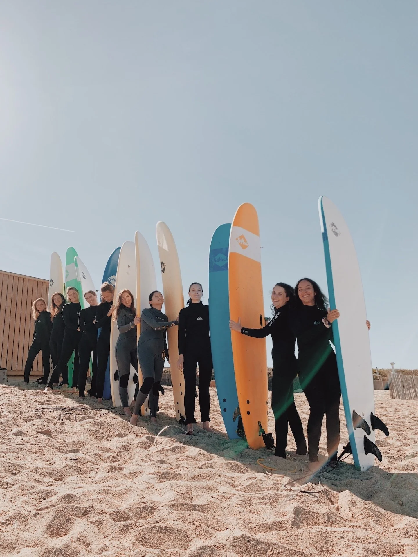 Groupe de participantes en combinaison alignées sur la plage, planches de surf à la main — esprit collectif d'un surf camp yoga au Cap Ferret