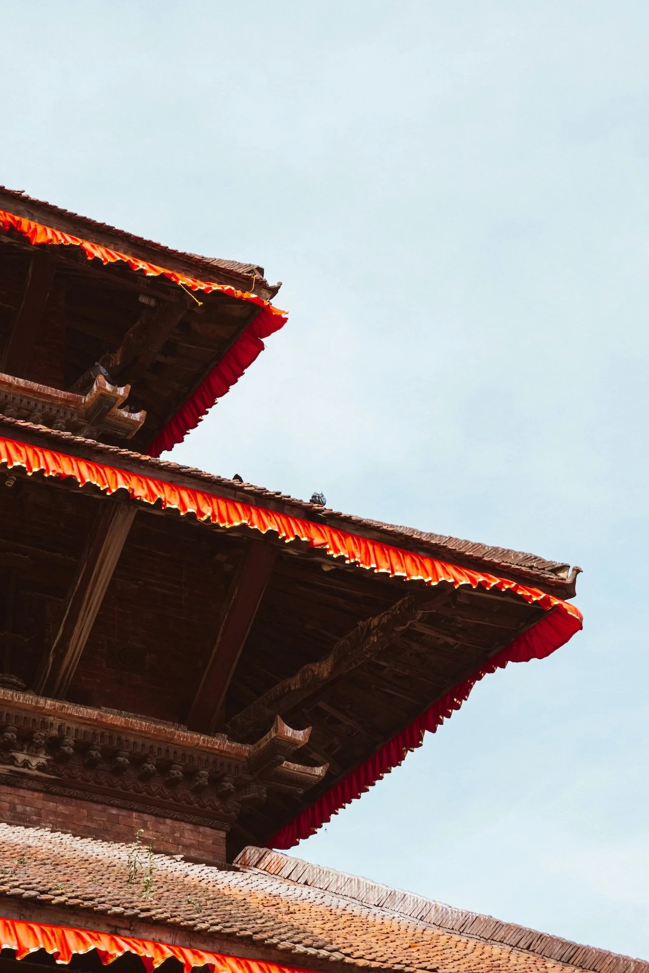 Angle architectural d'un temple en bois au Népal, bordures rouges sculptées se découpant sur le ciel — retraite spirituelle dans l'Himalaya