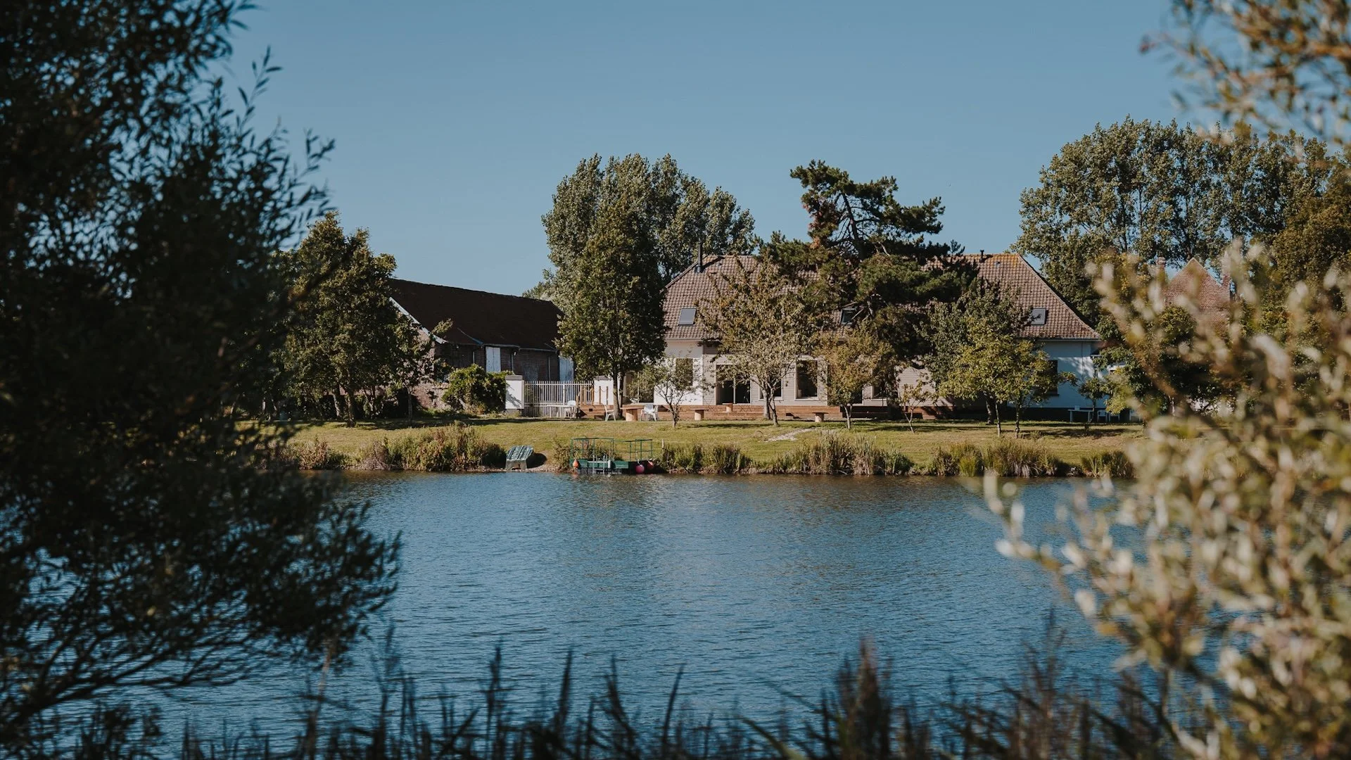 Vue paisible sur la grande maison de campagne depuis l'étang, entourée d'arbres dans la lumière de plein été — yoga dans la nature, Baie de Somme