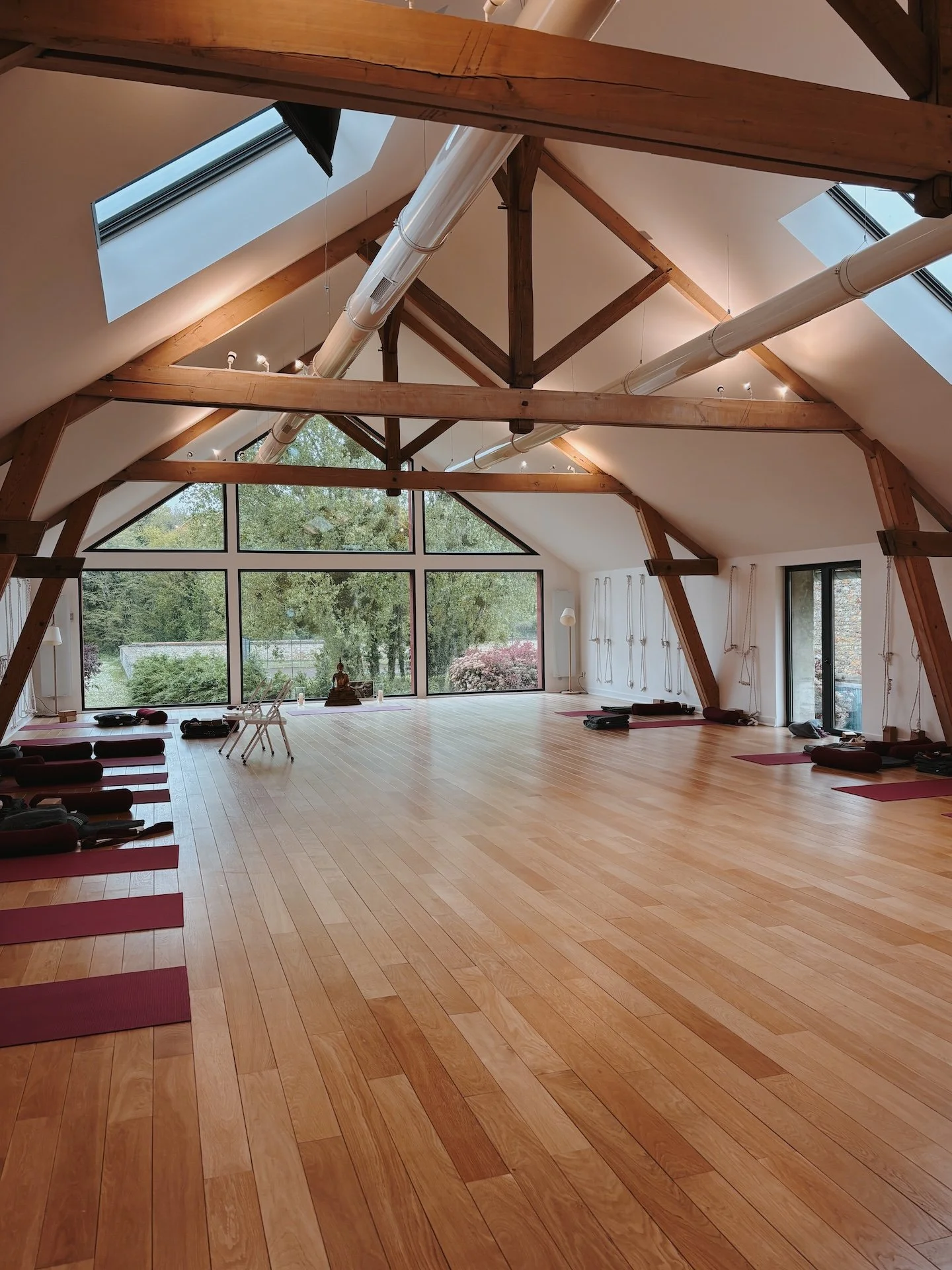 Salle de yoga avec charpente en bois et grandes baies vitrées ouvertes sur la nature — retraite yoga Kundalini et chamanisme château de Solterre proche de Paris 2026