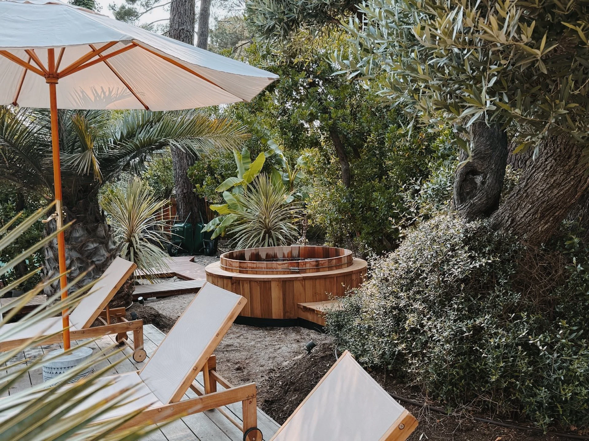 Coin détente du jardin avec bain nordique en bois et transats entourés de verdure — pause bien-être lors d'une retraite yoga et surf